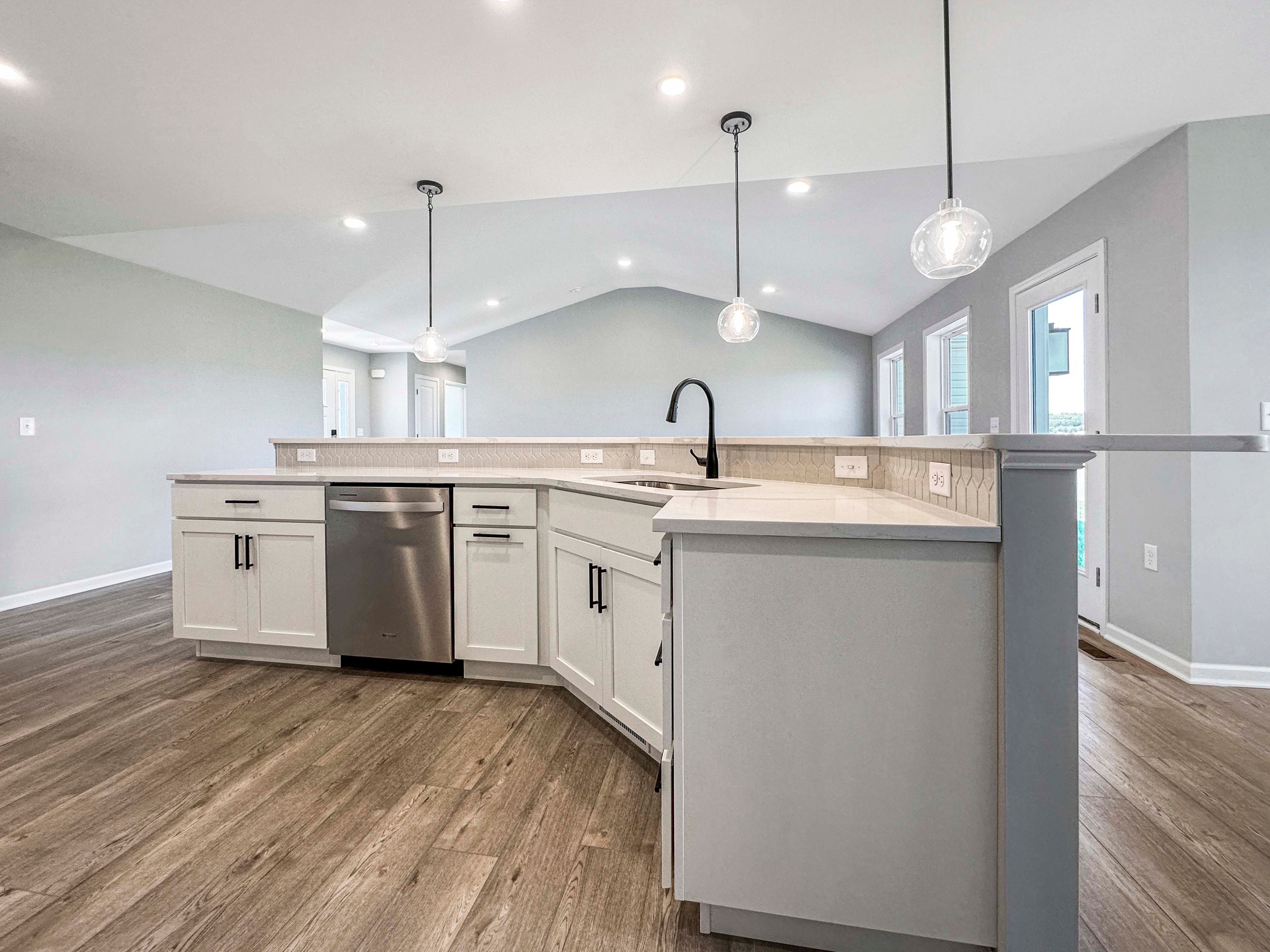 Spacious kitchen island with quartz countertops, a black faucet, and three clear pendant lights hanging above, surrounded by white cabinetry.