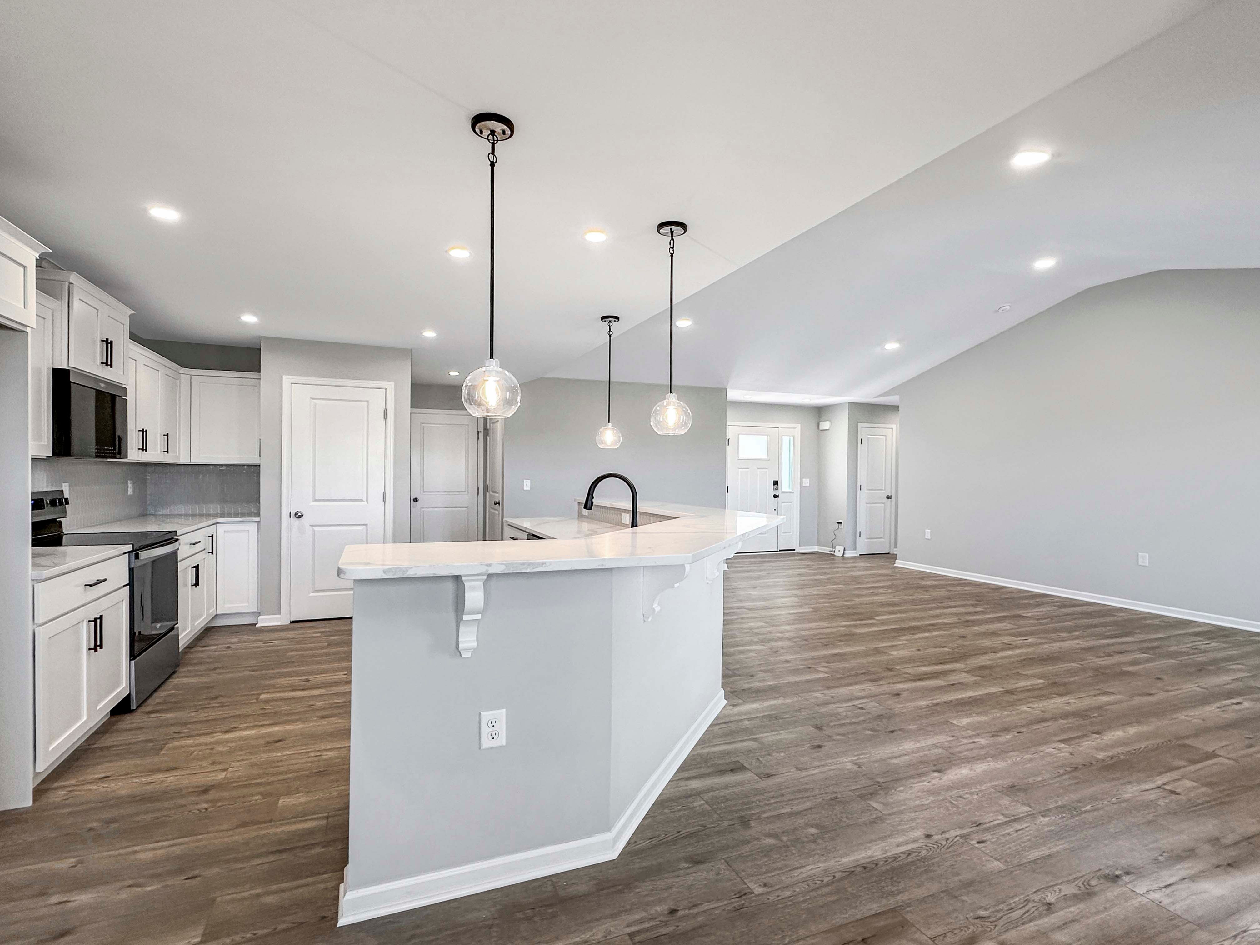 Open-concept kitchen with an expansive island, pendant lighting, and views into the great room with unfurnished space and vinyl plank flooring.