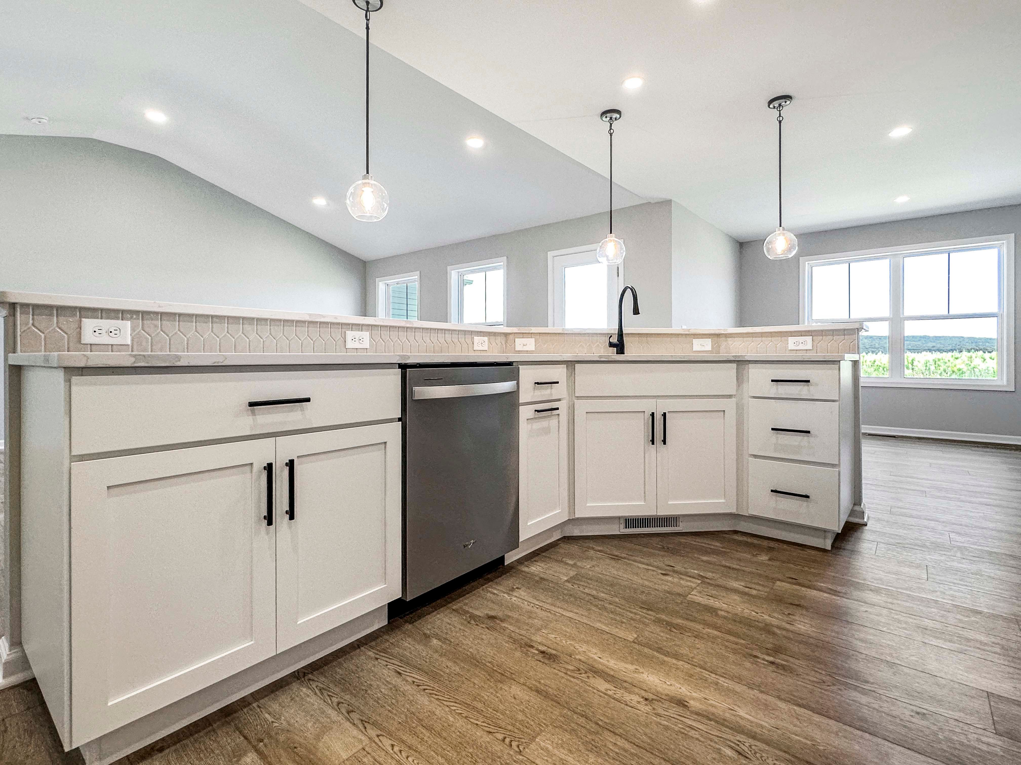 Angled view of large kitchen island with white cabinetry, built-in dishwasher, and three clear pendant lights hanging overhead.