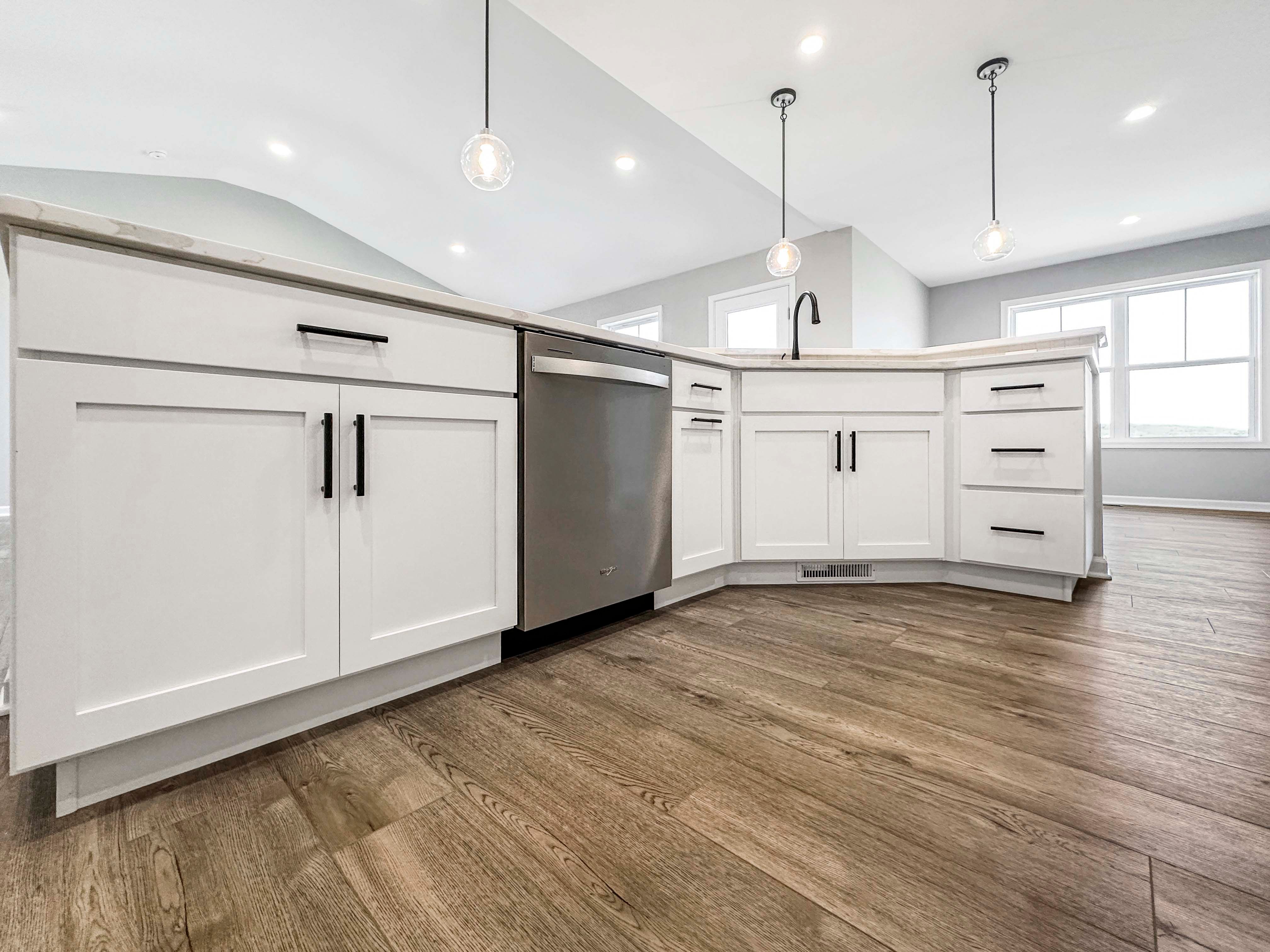 Kitchen island with curved seating area, white cabinetry, and contrasting black hardware, highlighted by a trio of glass pendant lights.
