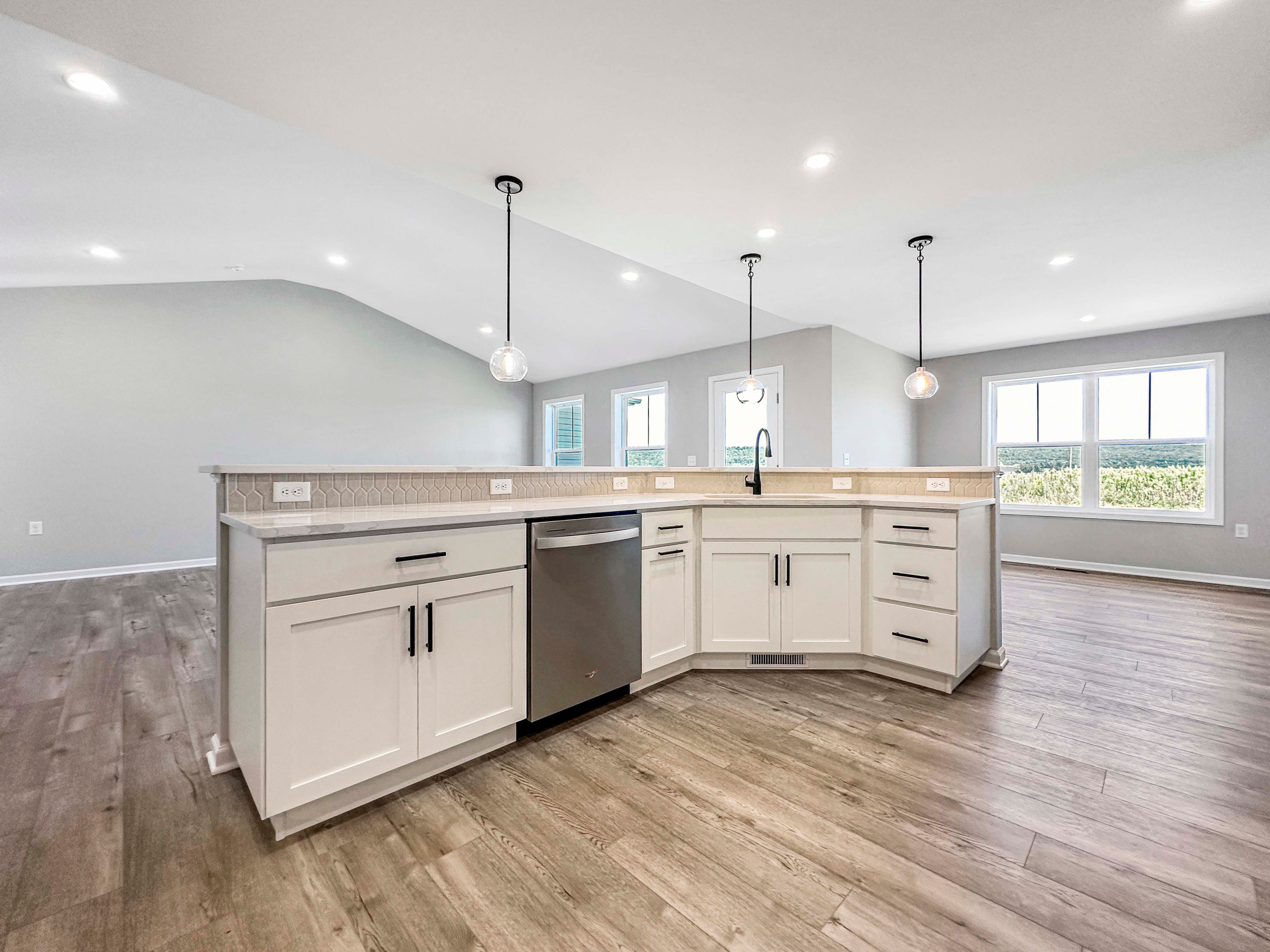 Lower view of kitchen island with white shaker cabinets and black hardware, quartz countertops, and an integrated dishwasher.