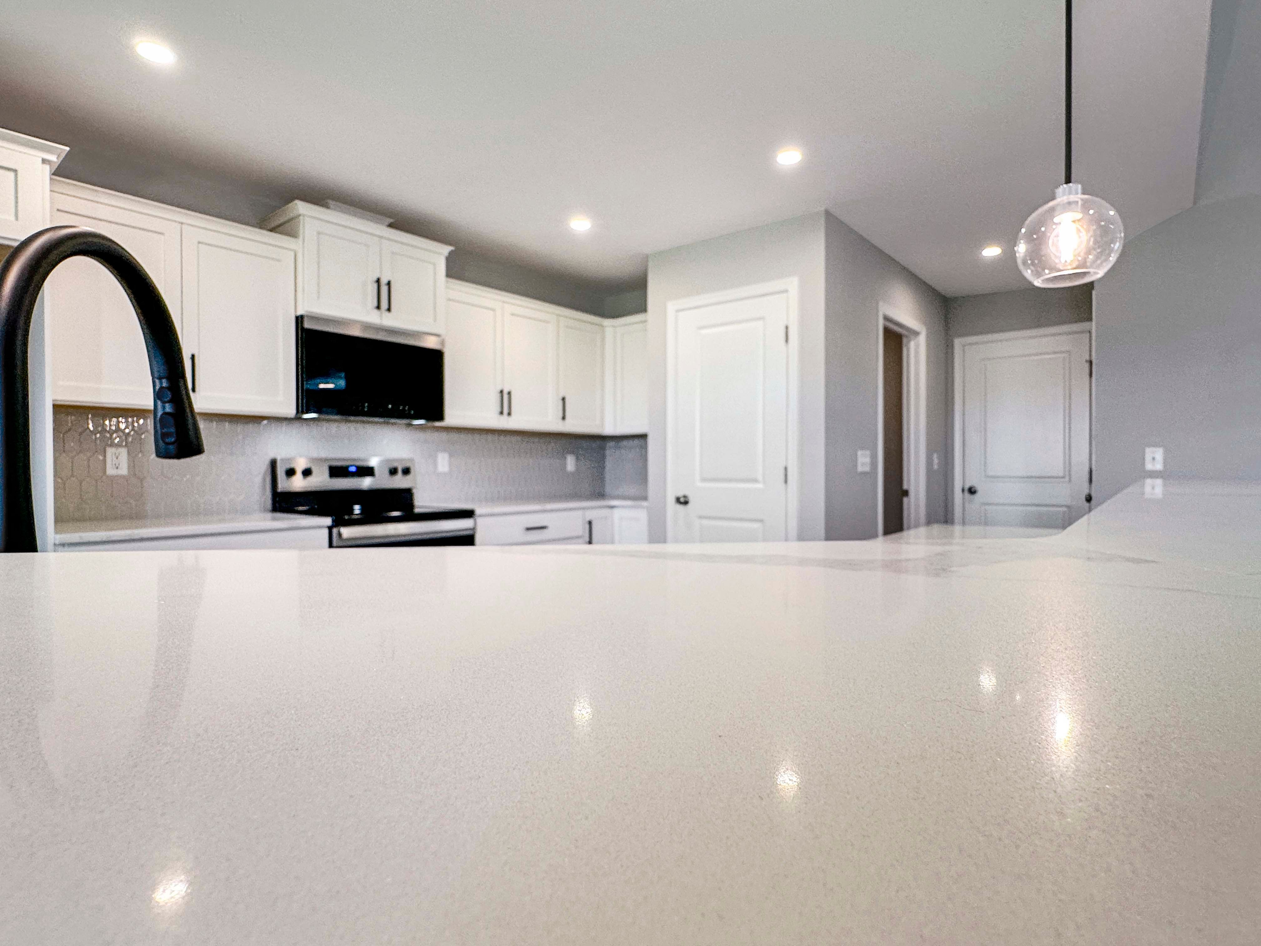 Close-up of glossy hexagon-shaped backsplash tiles in light gray, complementing the quartz countertops in a modern kitchen.