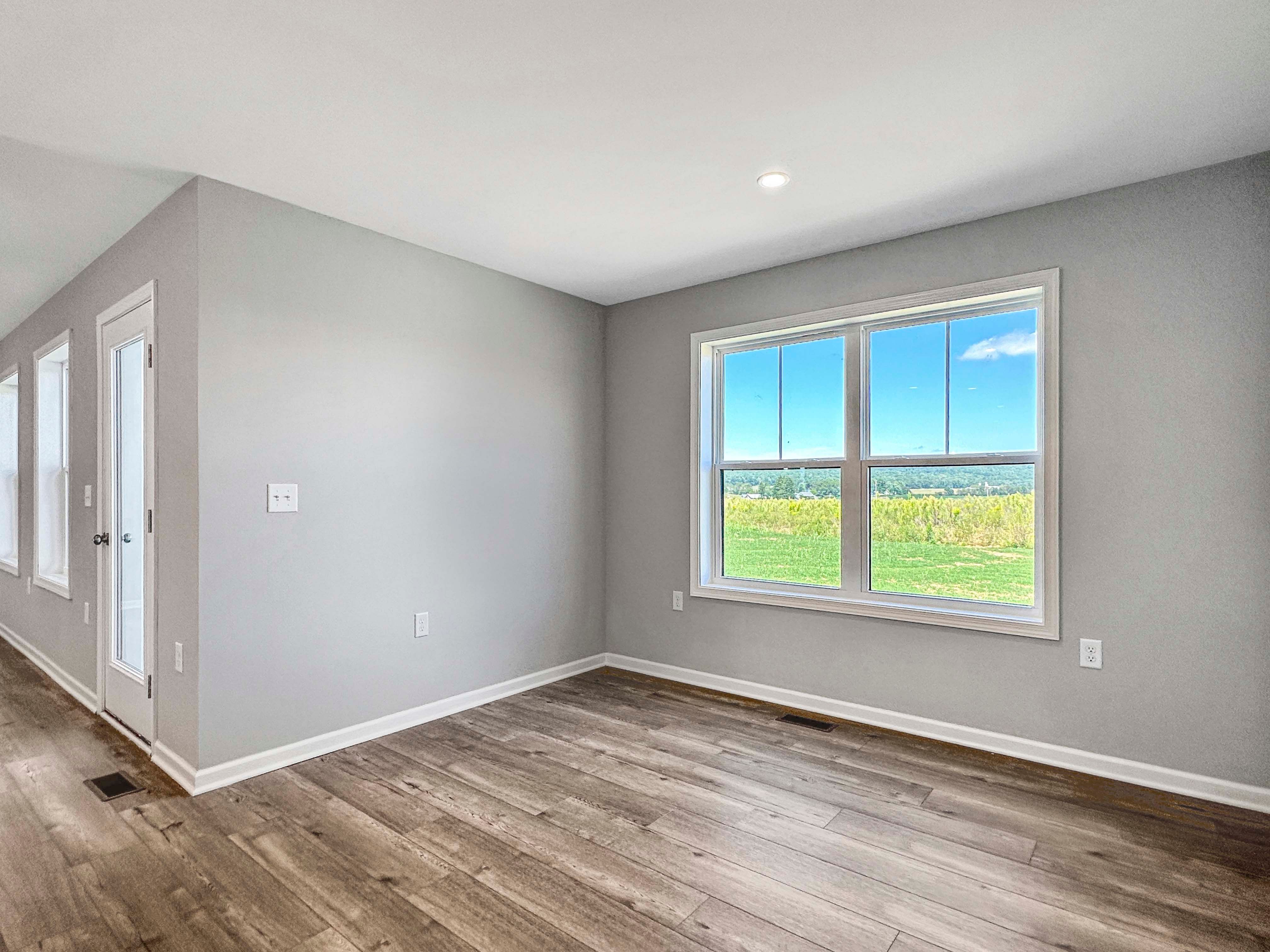 Bright breakfast area with large windows providing views of greenery. Wood-like flooring and neutral wall tones.