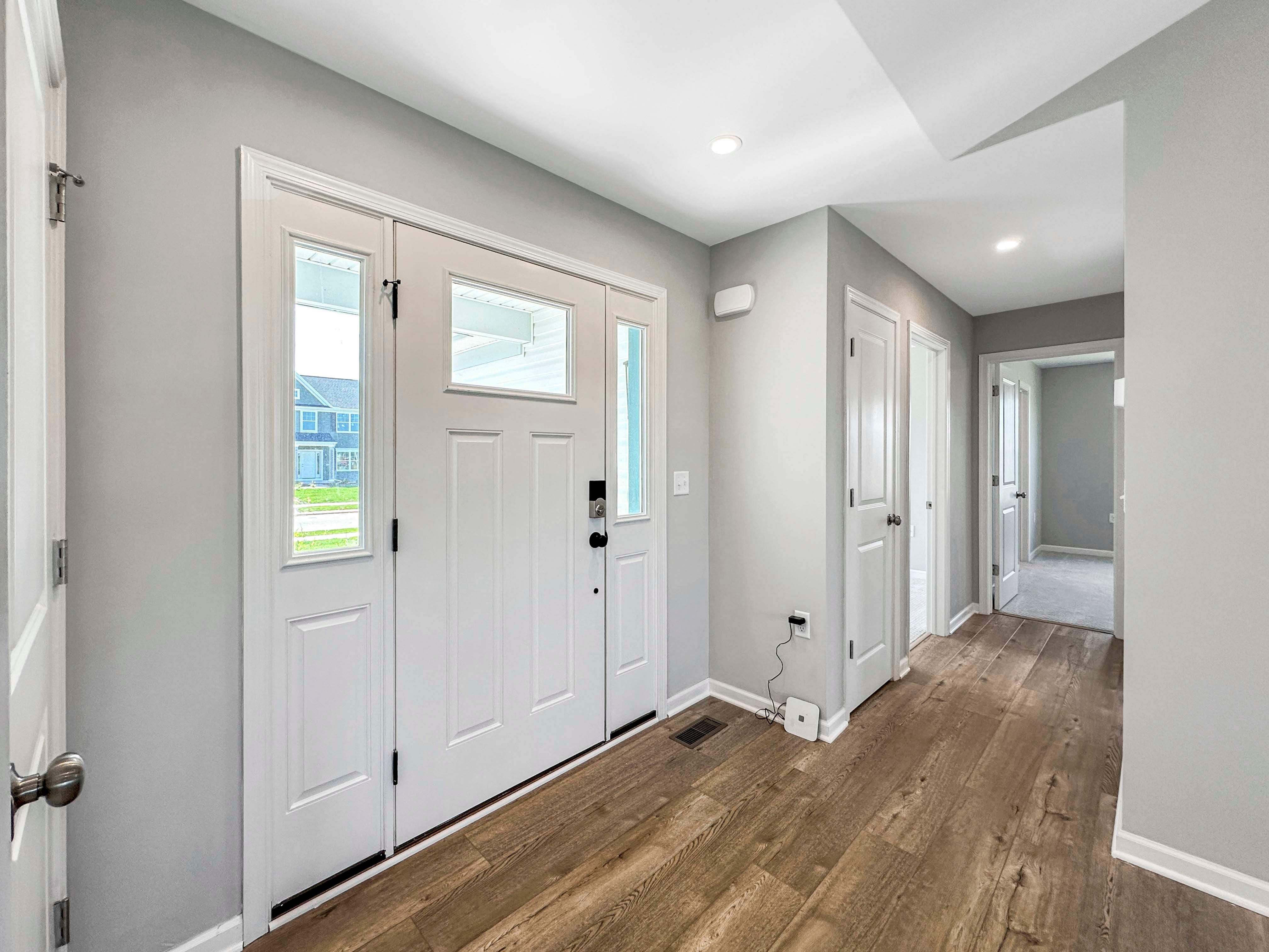 Entry foyer with wood-like flooring and a white front door featuring glass inserts. Hallway leading to bedrooms.