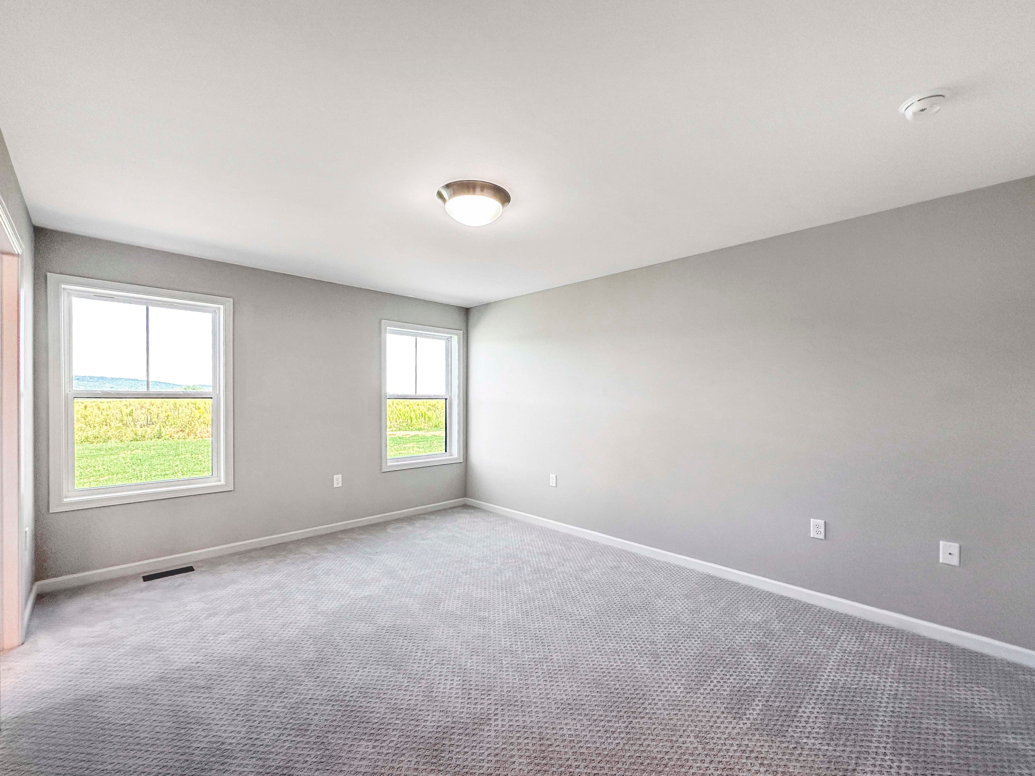 Owners bedroom with soft gray carpet, two large windows with scenic outdoor views, and multiple doorways to bathroom and closet.