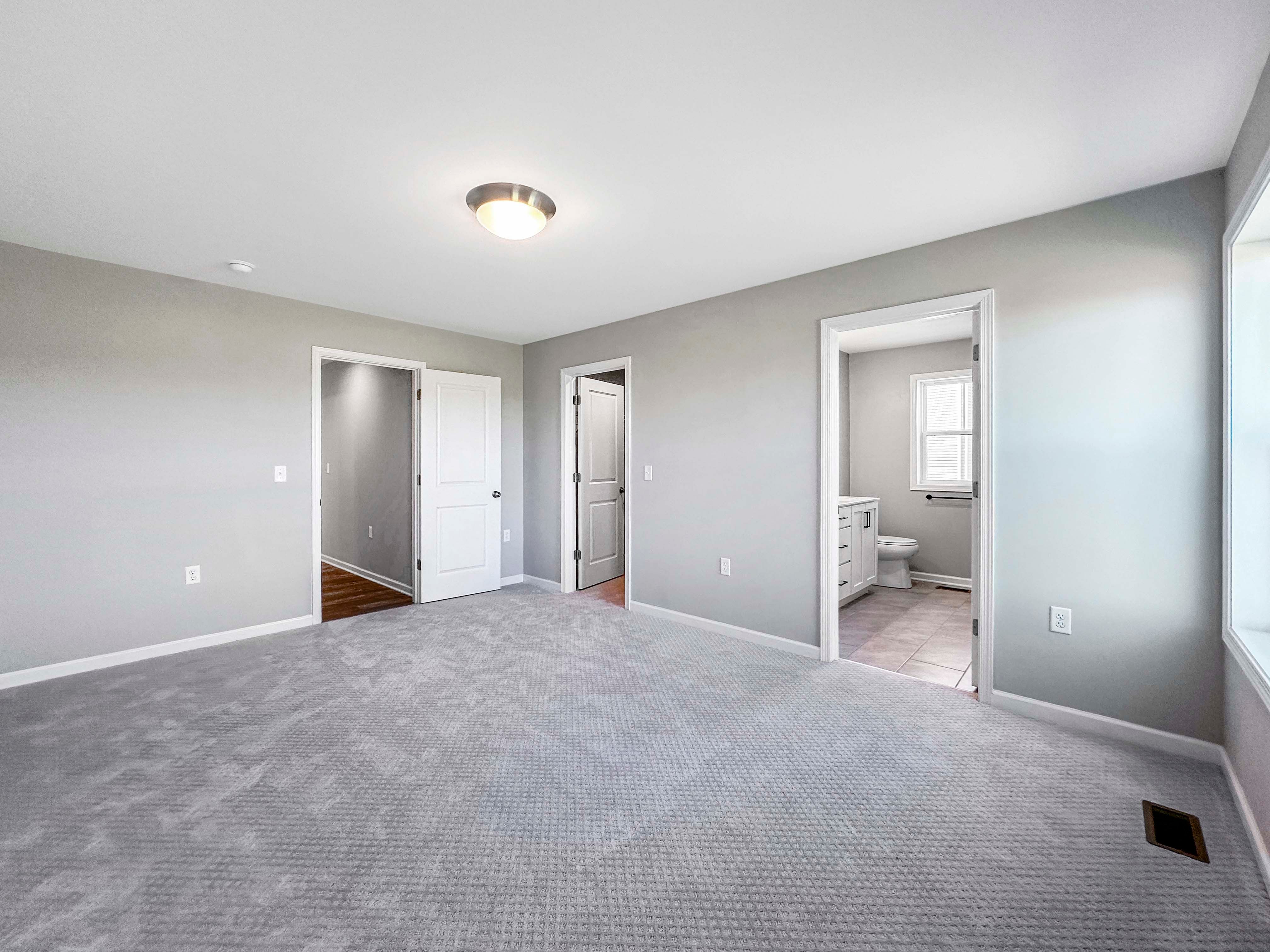Owners bedroom featuring gray carpet, open doorways to the ensuite bath and walk-in closet, with natural light from the windows.