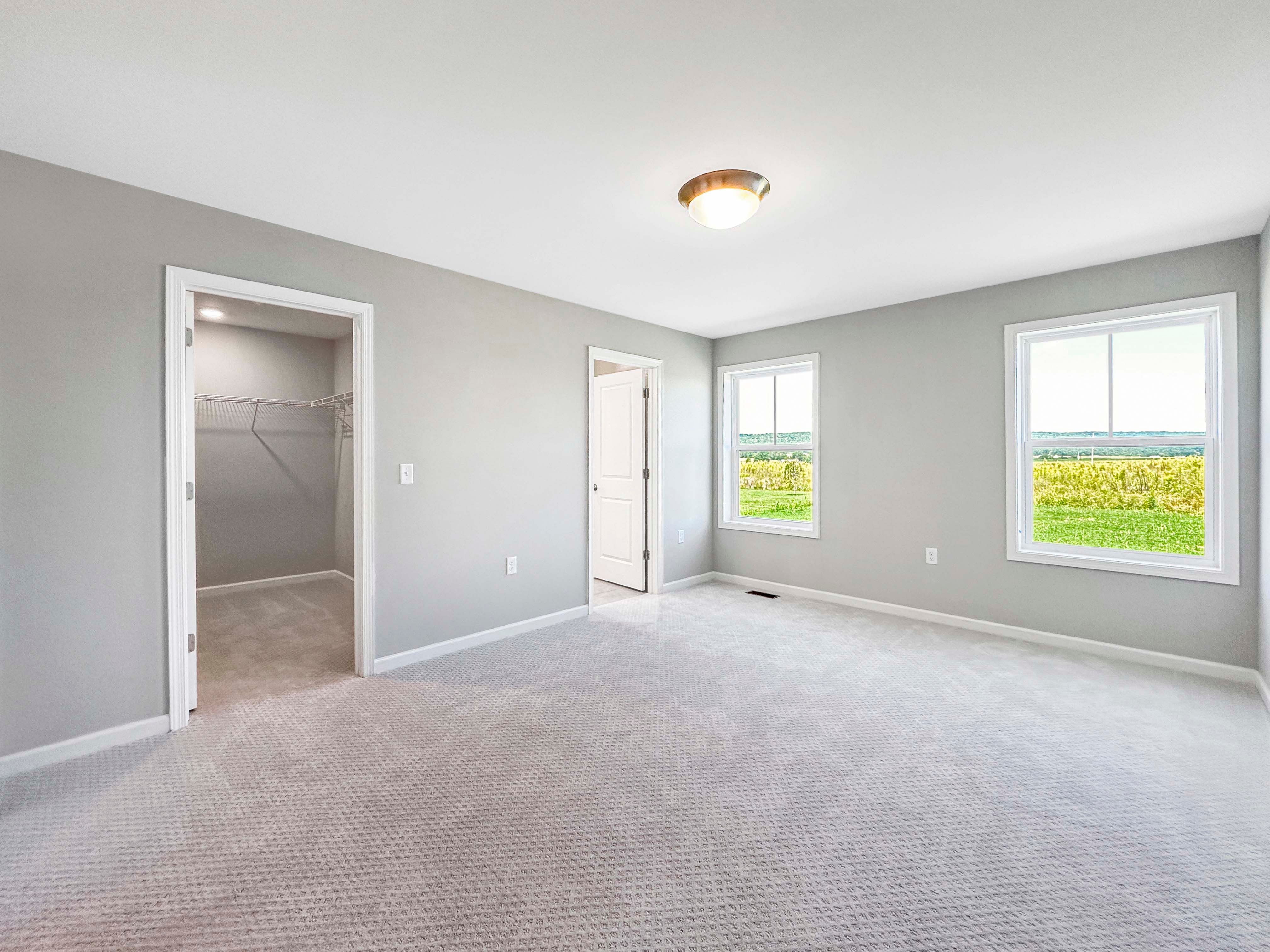 Spacious owners bedroom with plush carpet, two windows overlooking greenery, and an open doorway leading to the ensuite bathroom.
