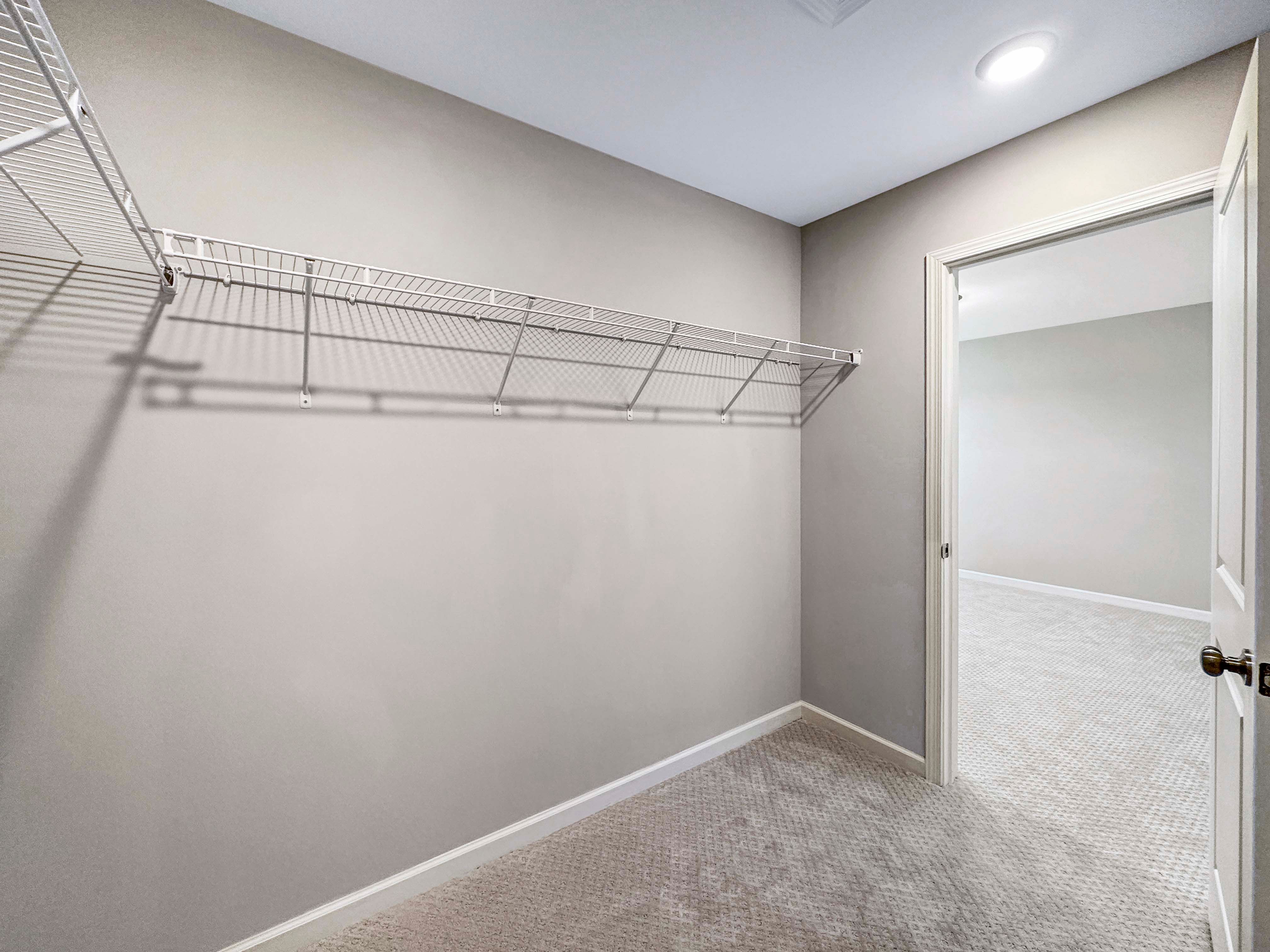 Walk-in closet with wire shelving and gray carpet, leading into the unfurnished owners bedroom.