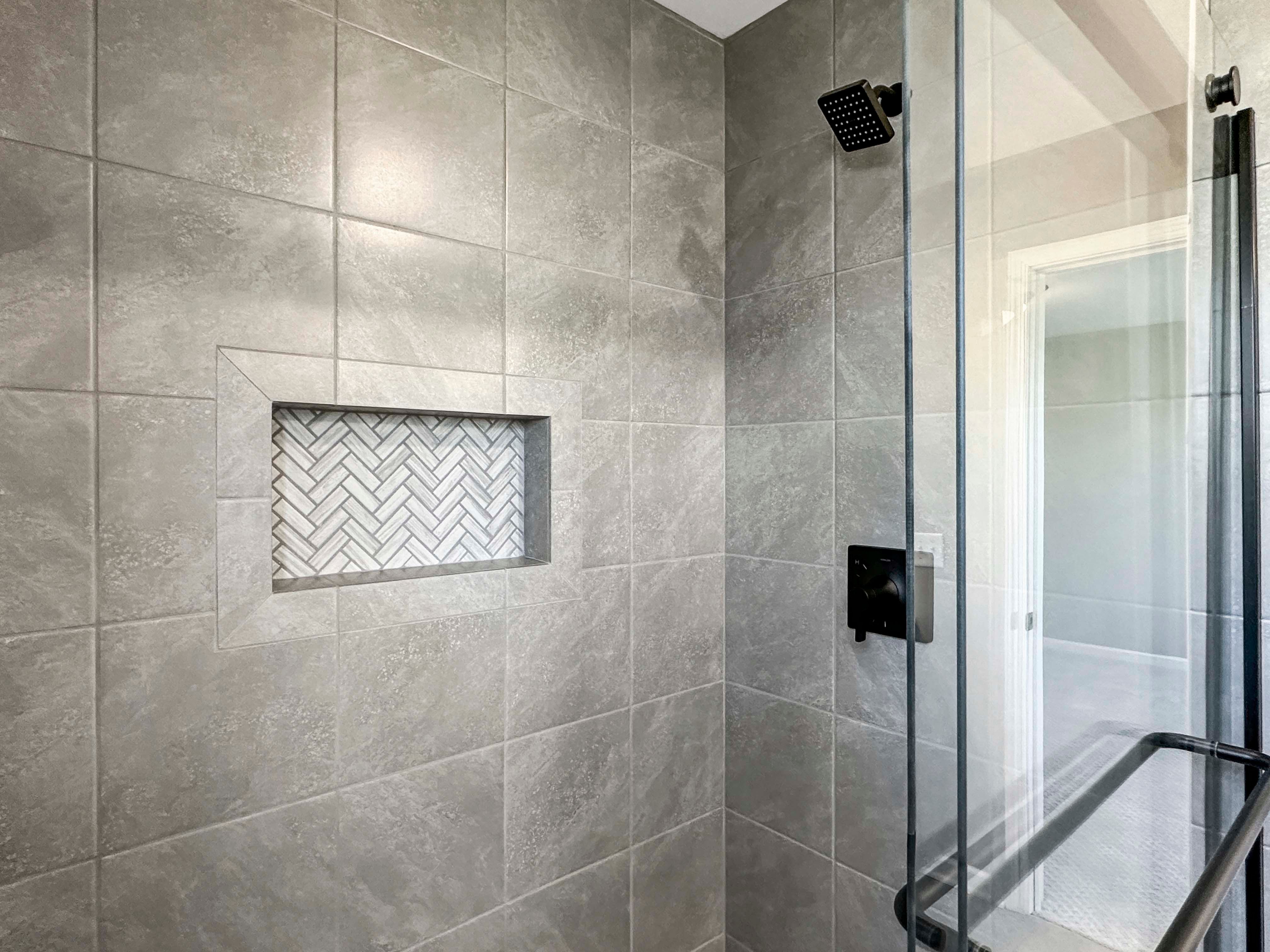 Modern shower with large gray tiles and a recessed niche with herringbone tile pattern, featuring black hardware.