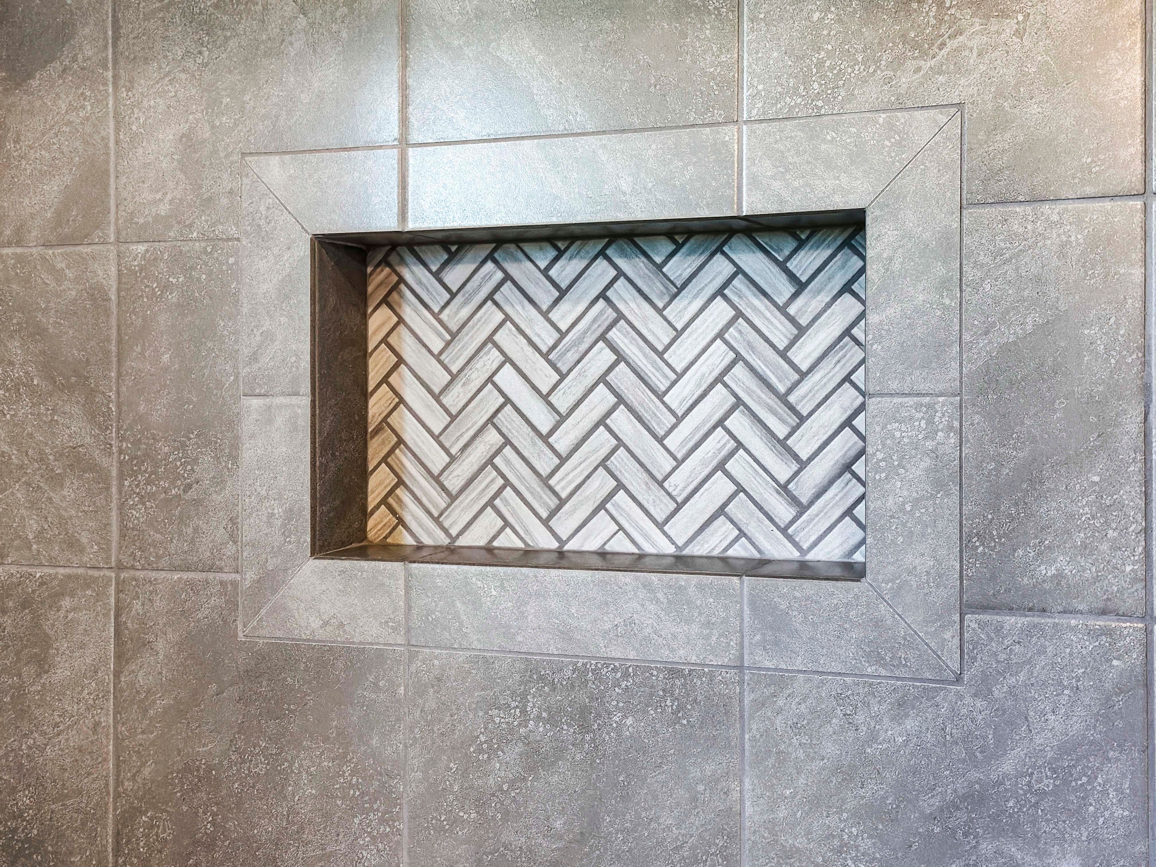 Close-up of a recessed niche with herringbone tile pattern, surrounded by large gray shower tiles.