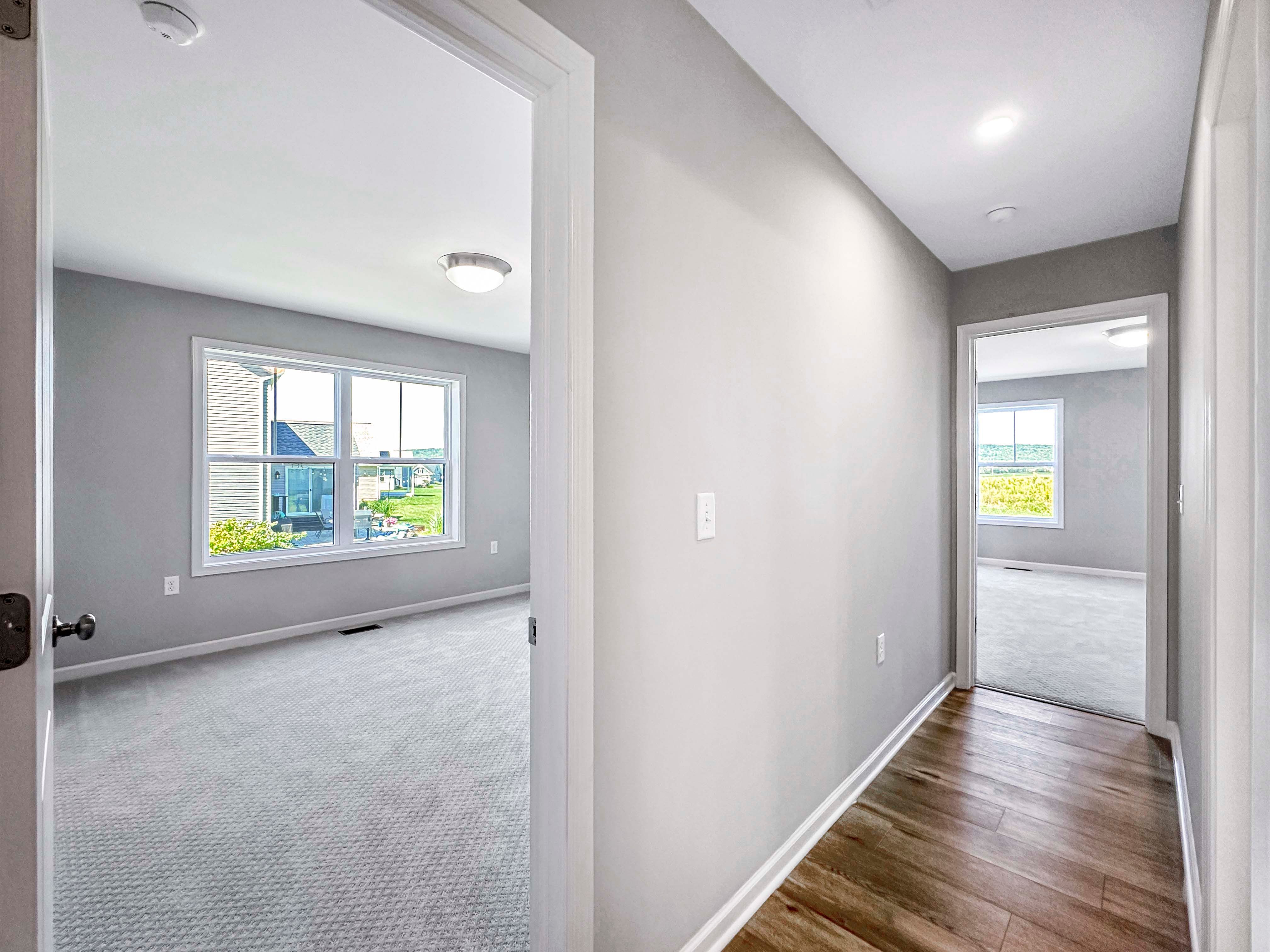 Hallway leading to two bedrooms, one with a large window and natural light, wood-like flooring in the hall.