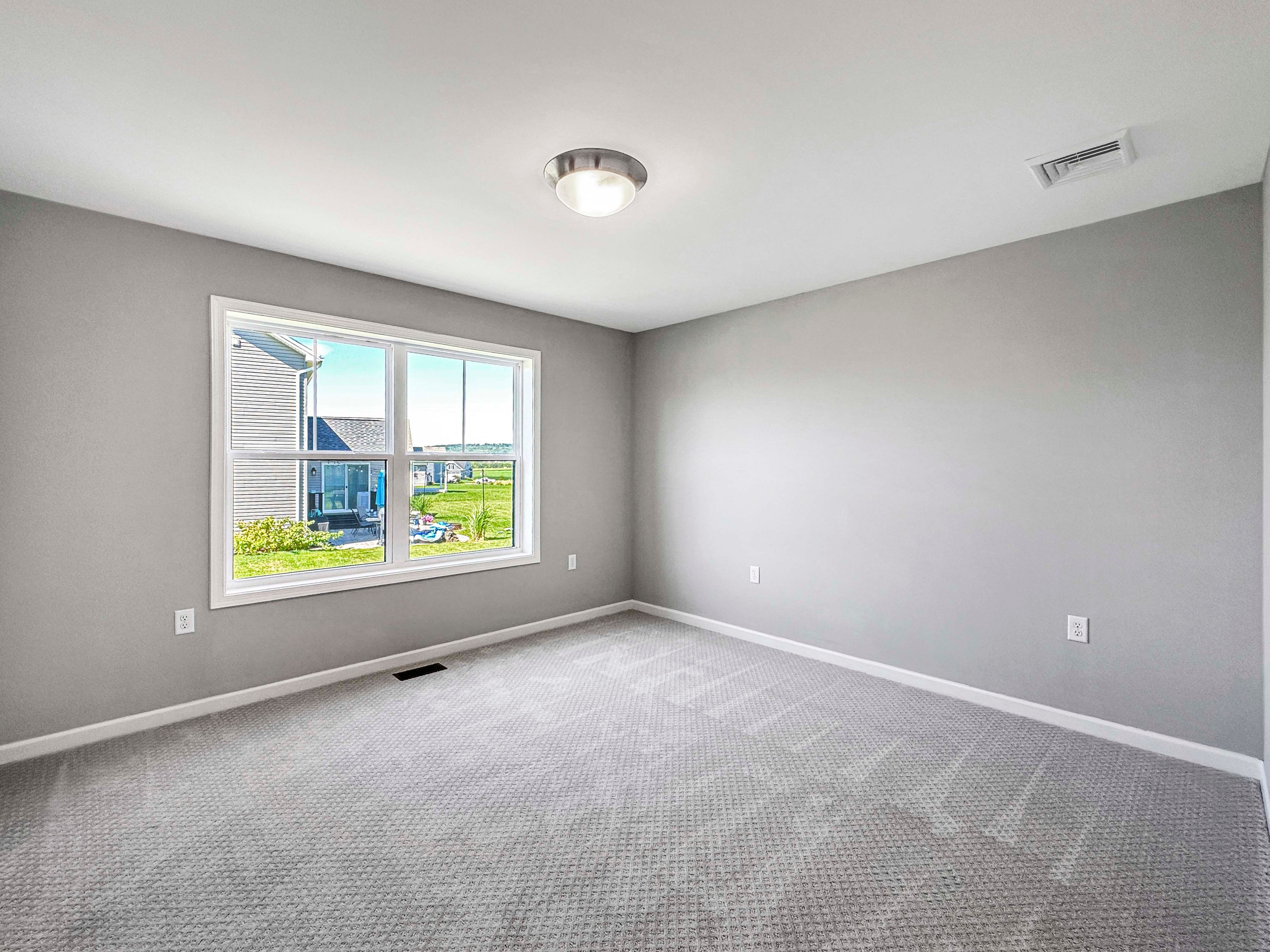 Unfurnished bedroom with neutral colors, gray carpet, and large windows allowing plenty of natural light.