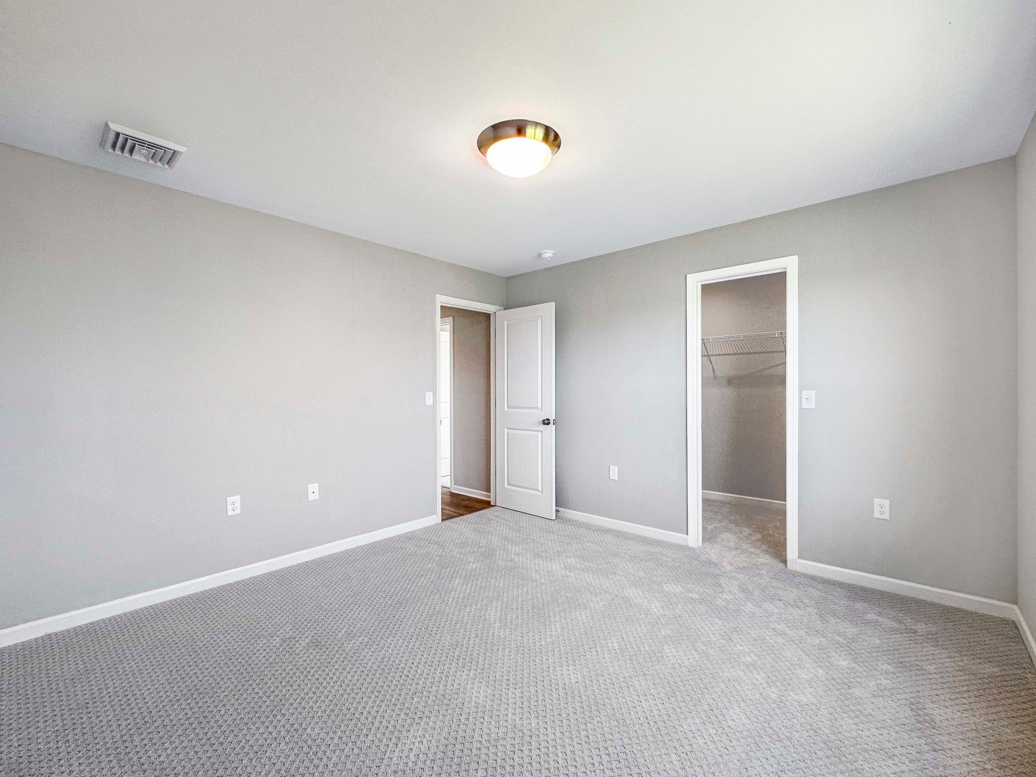 Bright bedroom with neutral gray walls, gray carpet, and natural light from large windows.
