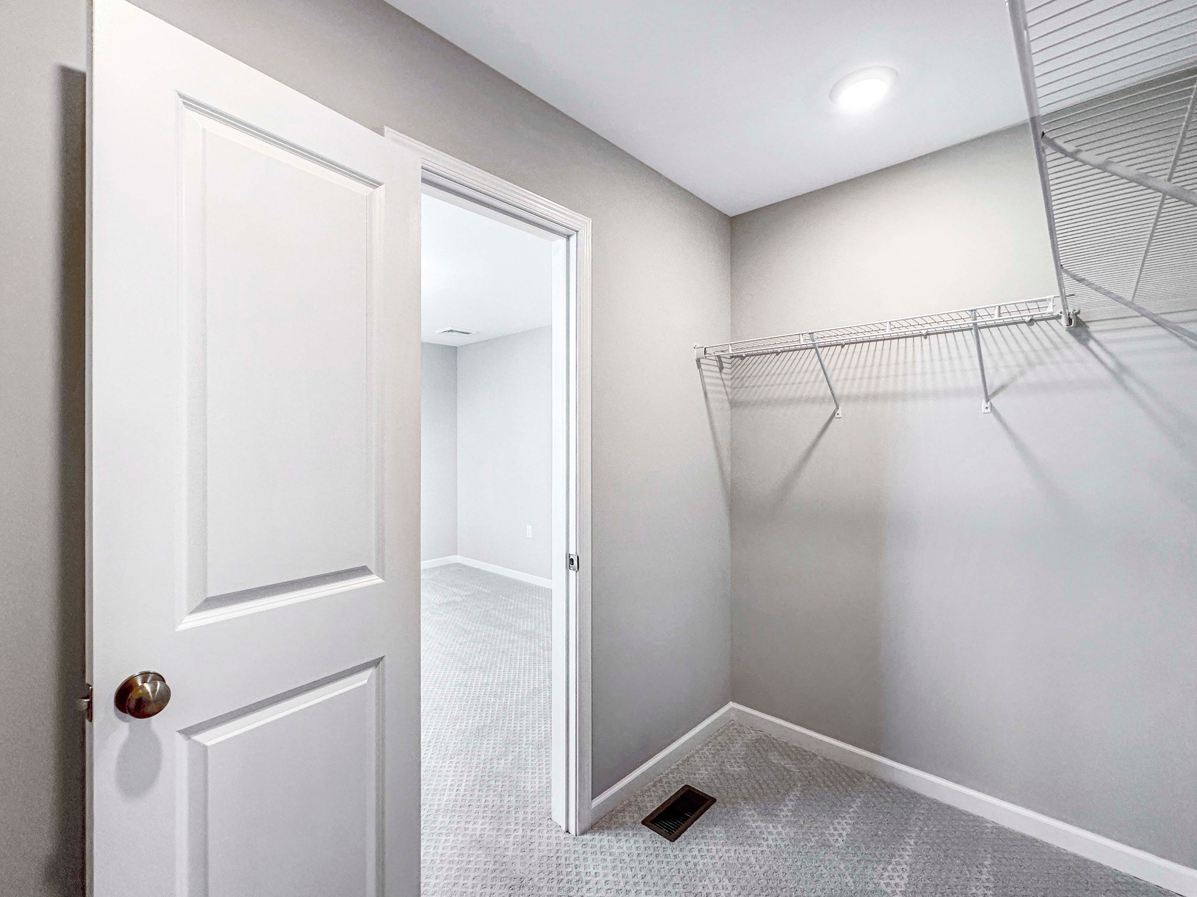 Unfurnished closet featuring wire shelving and carpet, leading out to the bedroom.