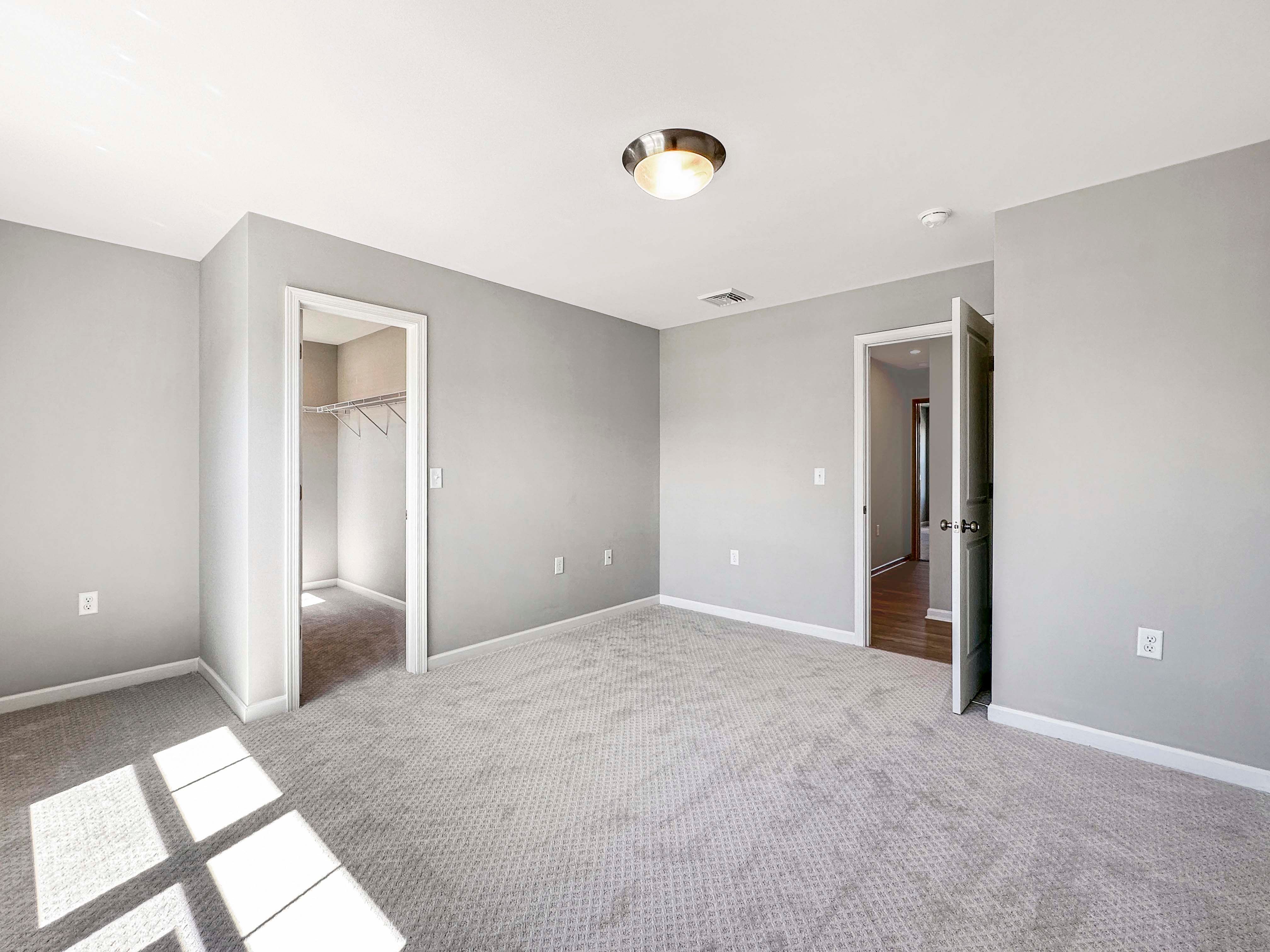 Unfurnished bedroom with neutral gray walls and carpet. Open closet and door leading to the hallway.