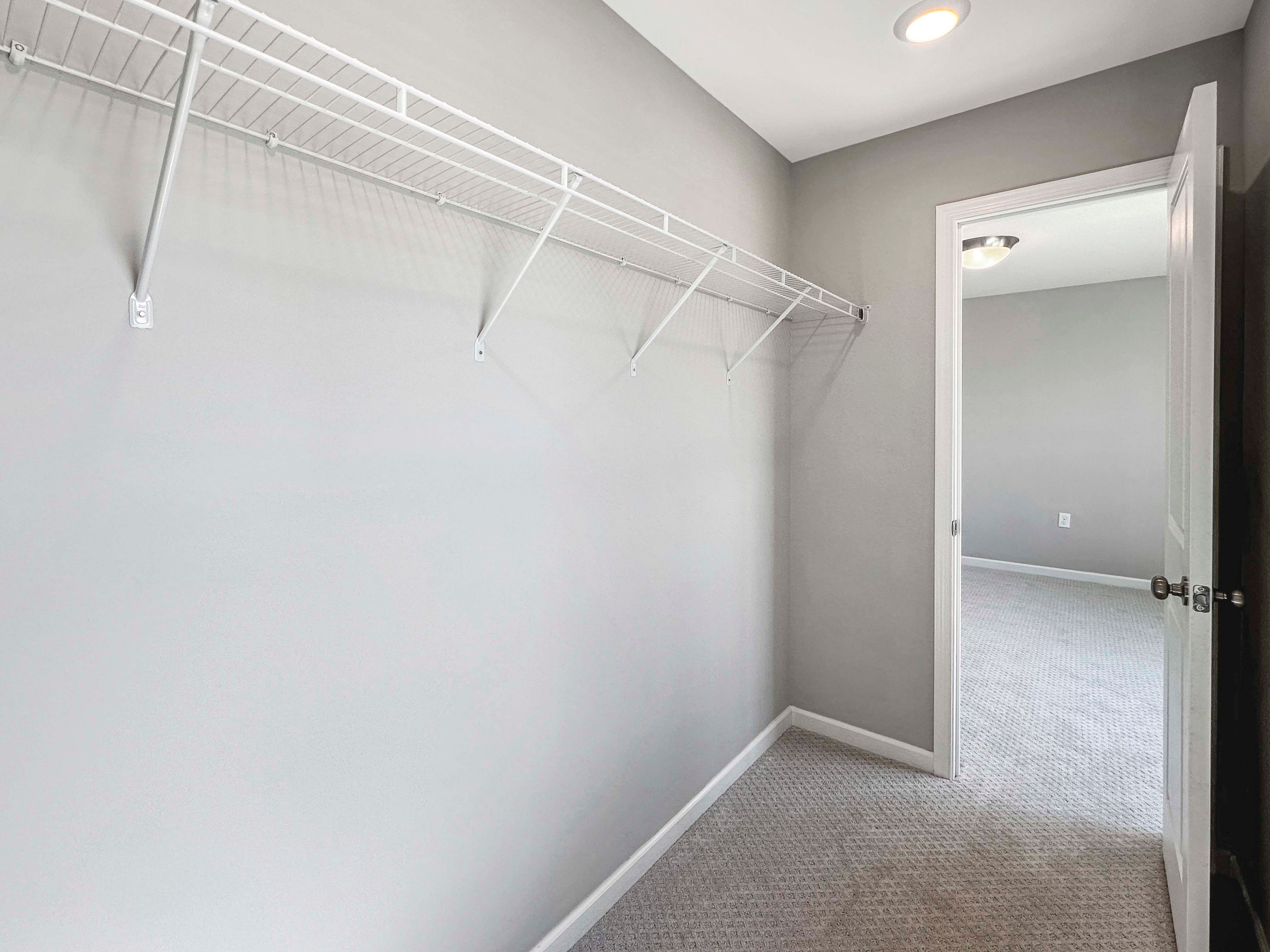 Walk-in closet with built-in wire shelving and a neutral palette. Carpet flooring and an open door leading to the bedroom.
