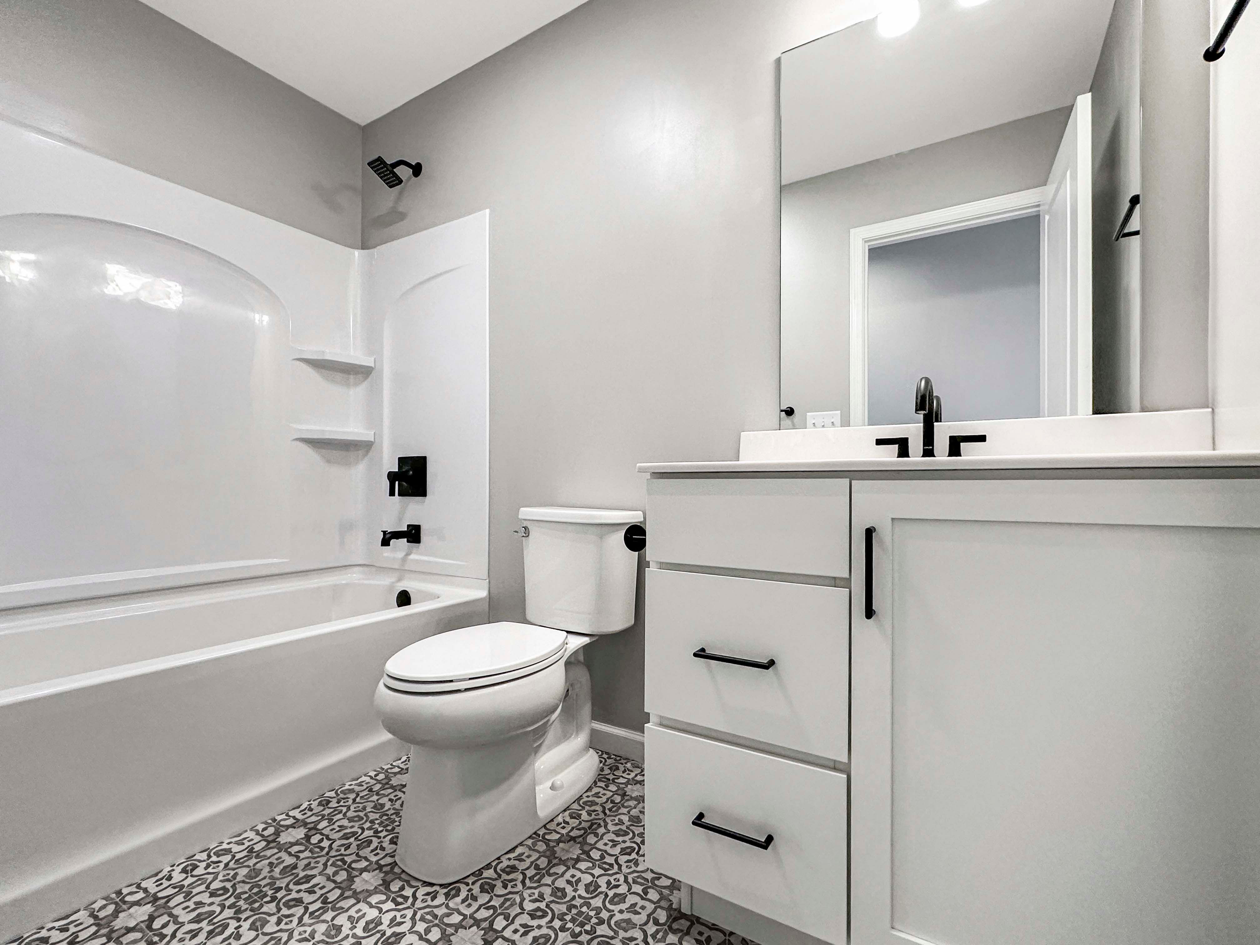 Full bathroom featuring a white tub, black fixtures, and white vanity with patterned tile flooring. Clean, modern design.