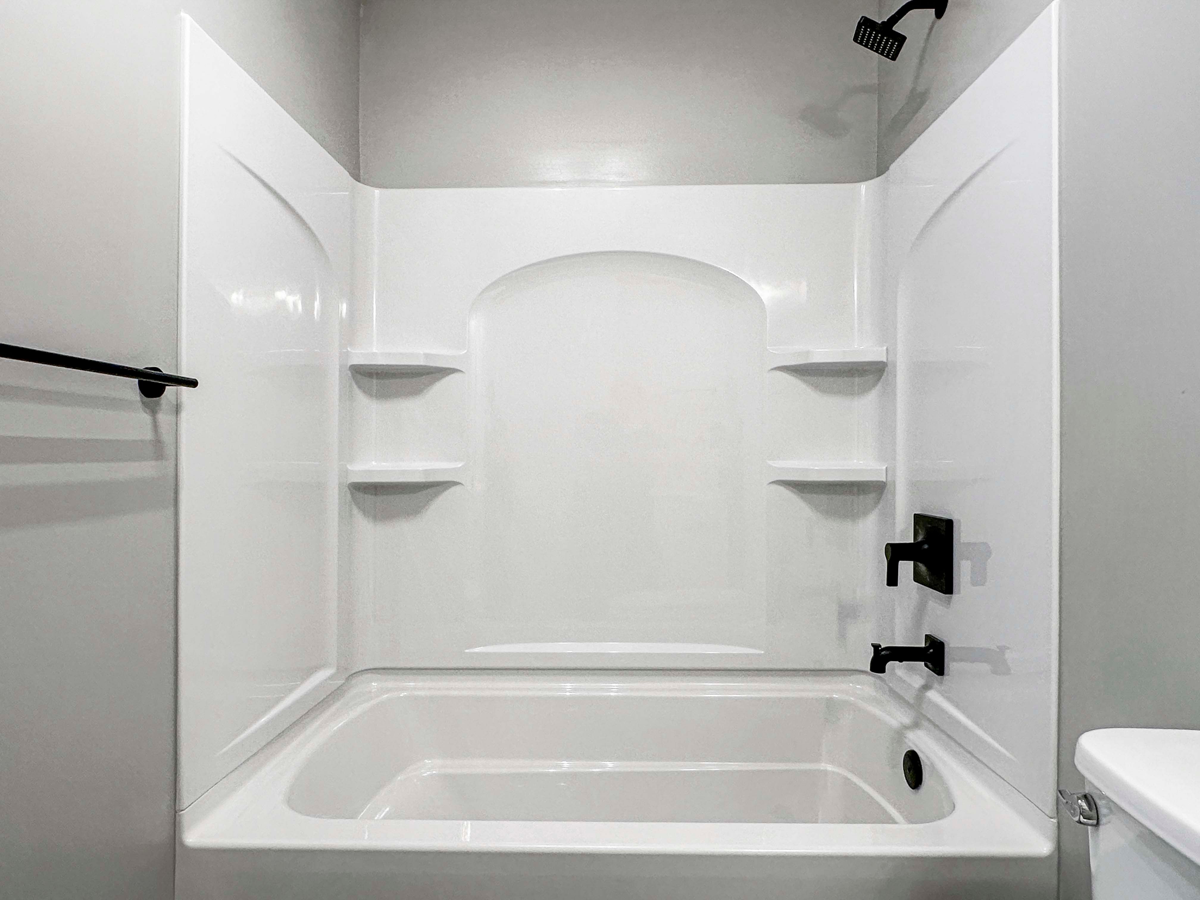 Close-up view of a white bathtub with black fixtures and built-in shelving. Modern, clean look with neutral tones.