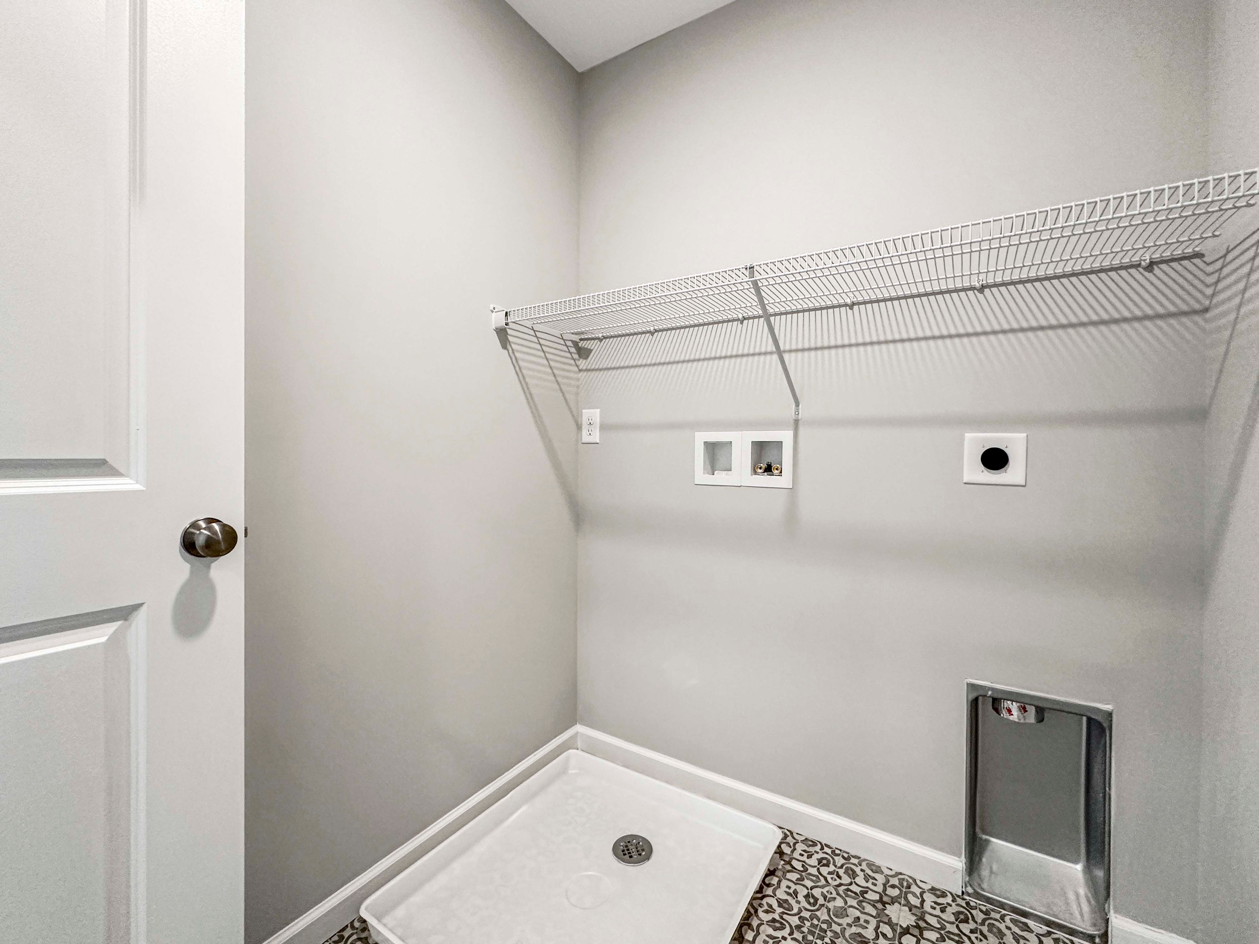 Unfurnished laundry room with patterned tile flooring, wire shelving, and plumbing hookups for washer and dryer.