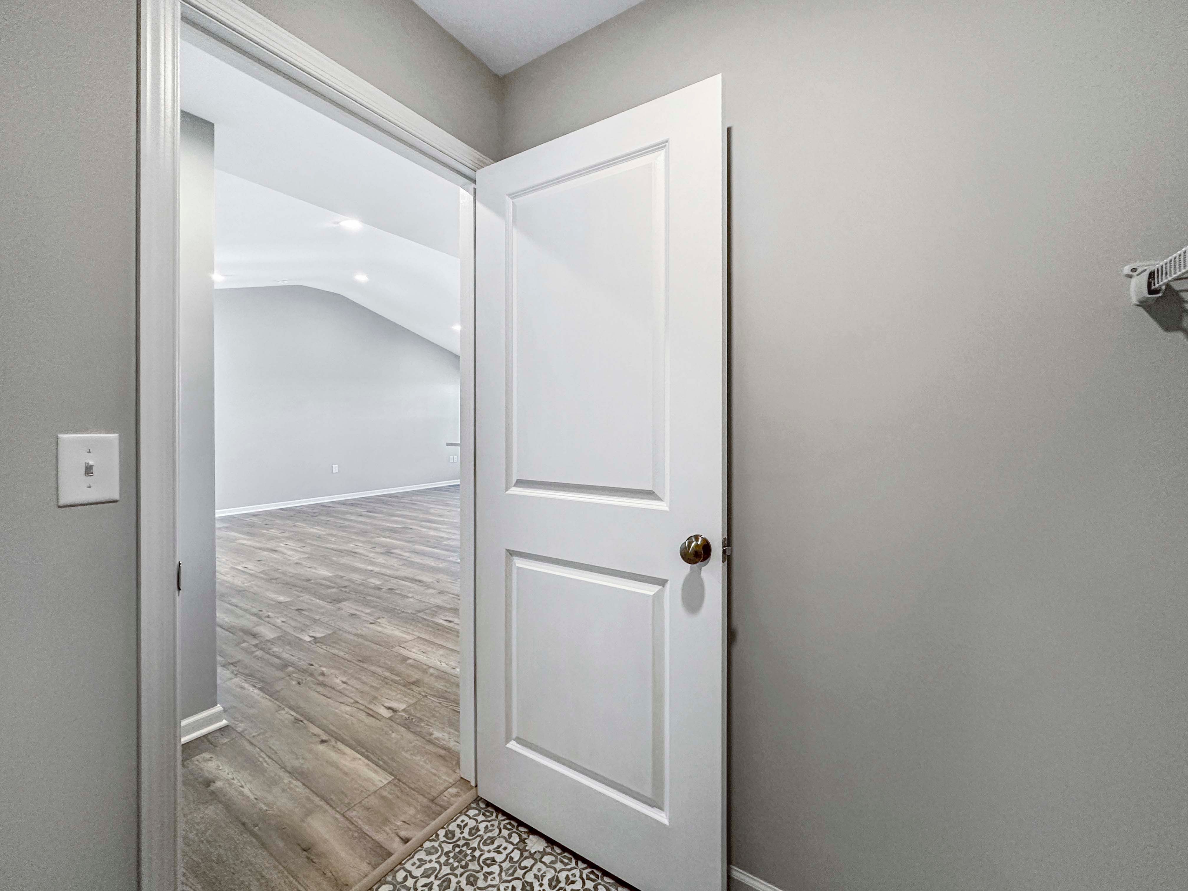 Laundry room view with open door leading to the main area, featuring patterned tile flooring and vinyl plank flooring beyond.