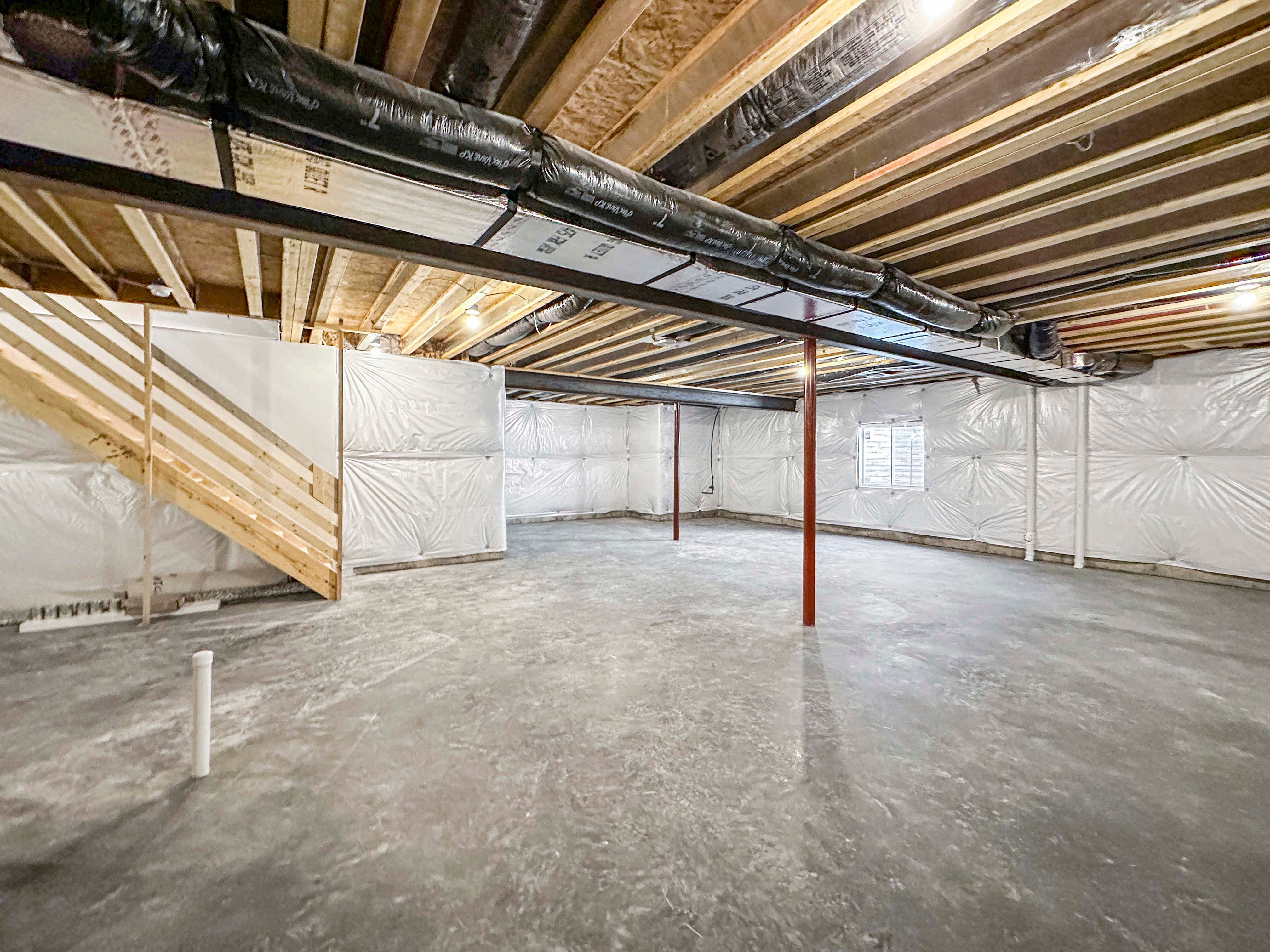 Spacious, unfurnished basement with exposed ceiling beams, utility equipment, and wooden stairs. Concrete floors and open space.