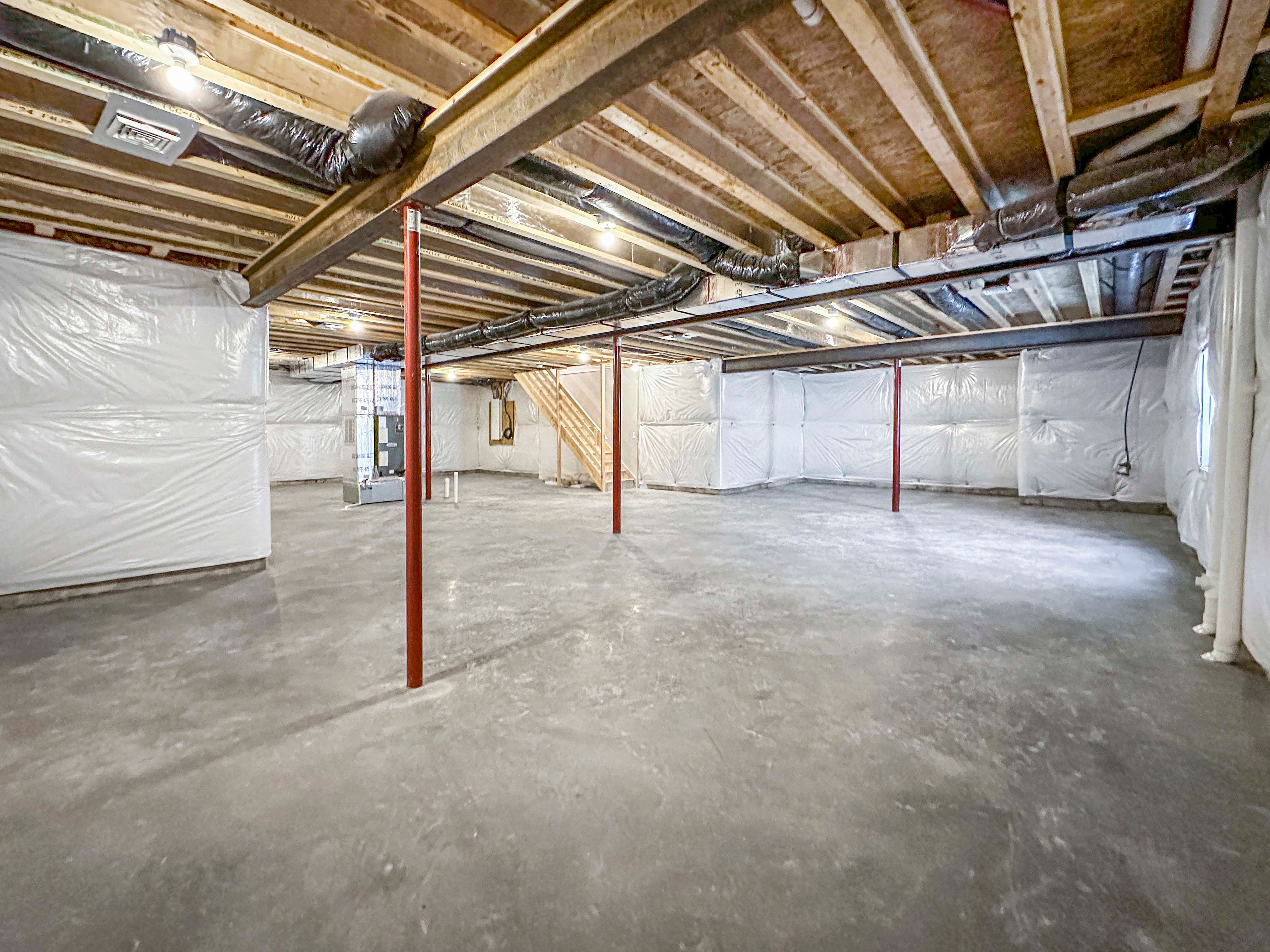 Spacious, unfurnished basement with exposed ceiling beams, concrete flooring, and ductwork. Natural light from side windows.
