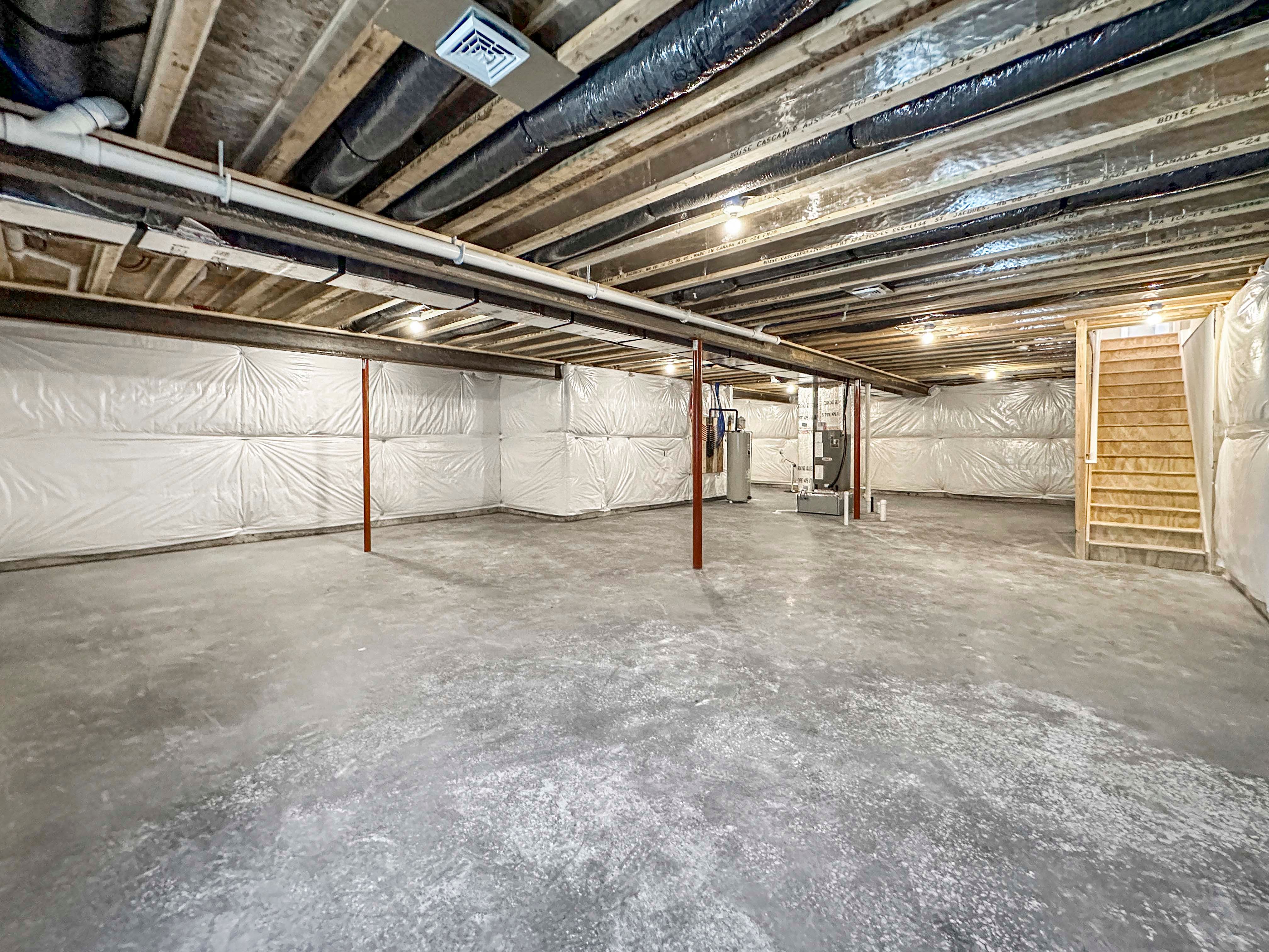 Large, unfinished basement with concrete floors, exposed ceiling beams, and ductwork. Open space with stairs leading up.