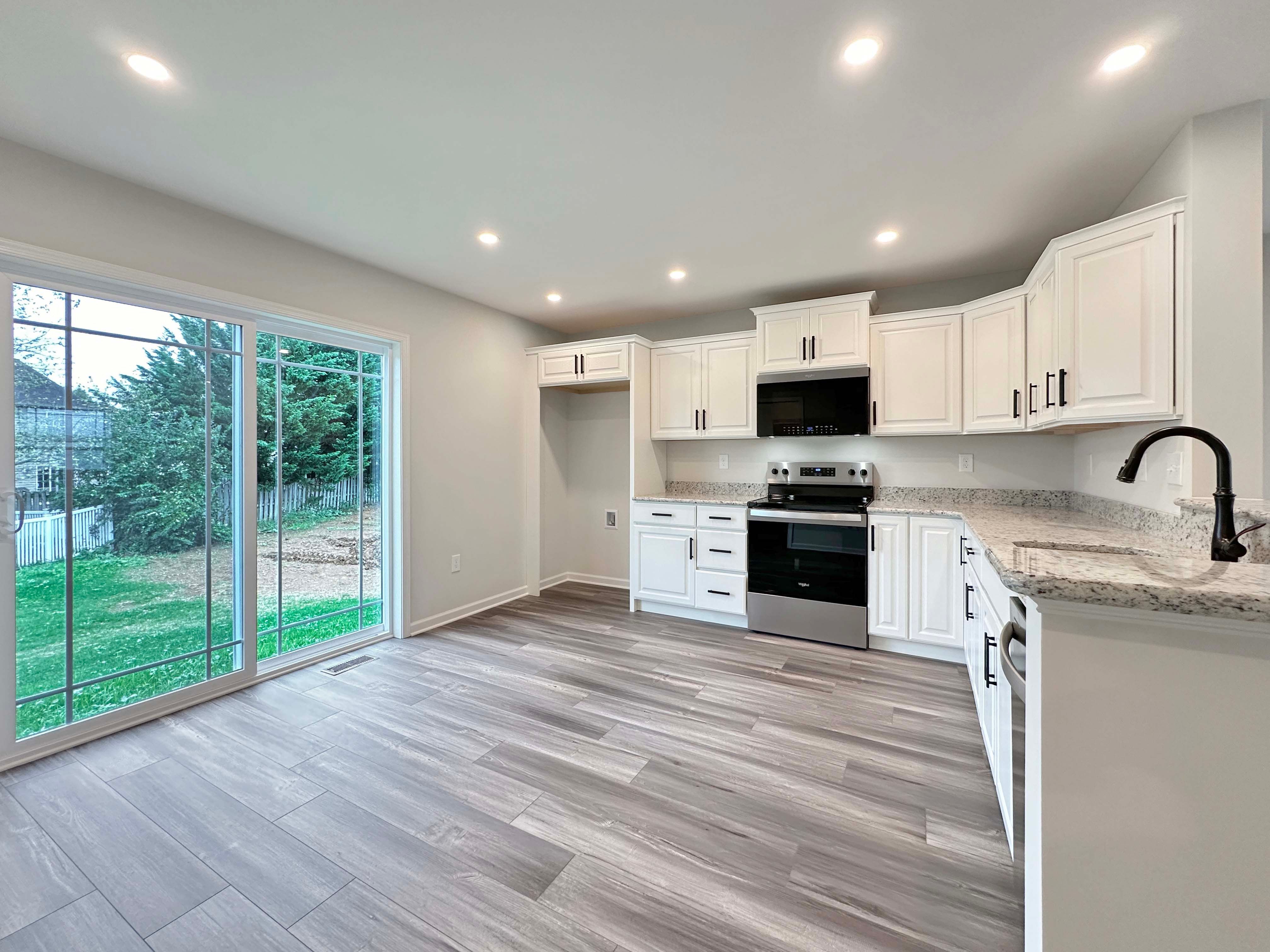 Bright kitchen with white cabinetry, granite countertops, and stainless-steel appliances. Sliding glass doors leading to back yard.