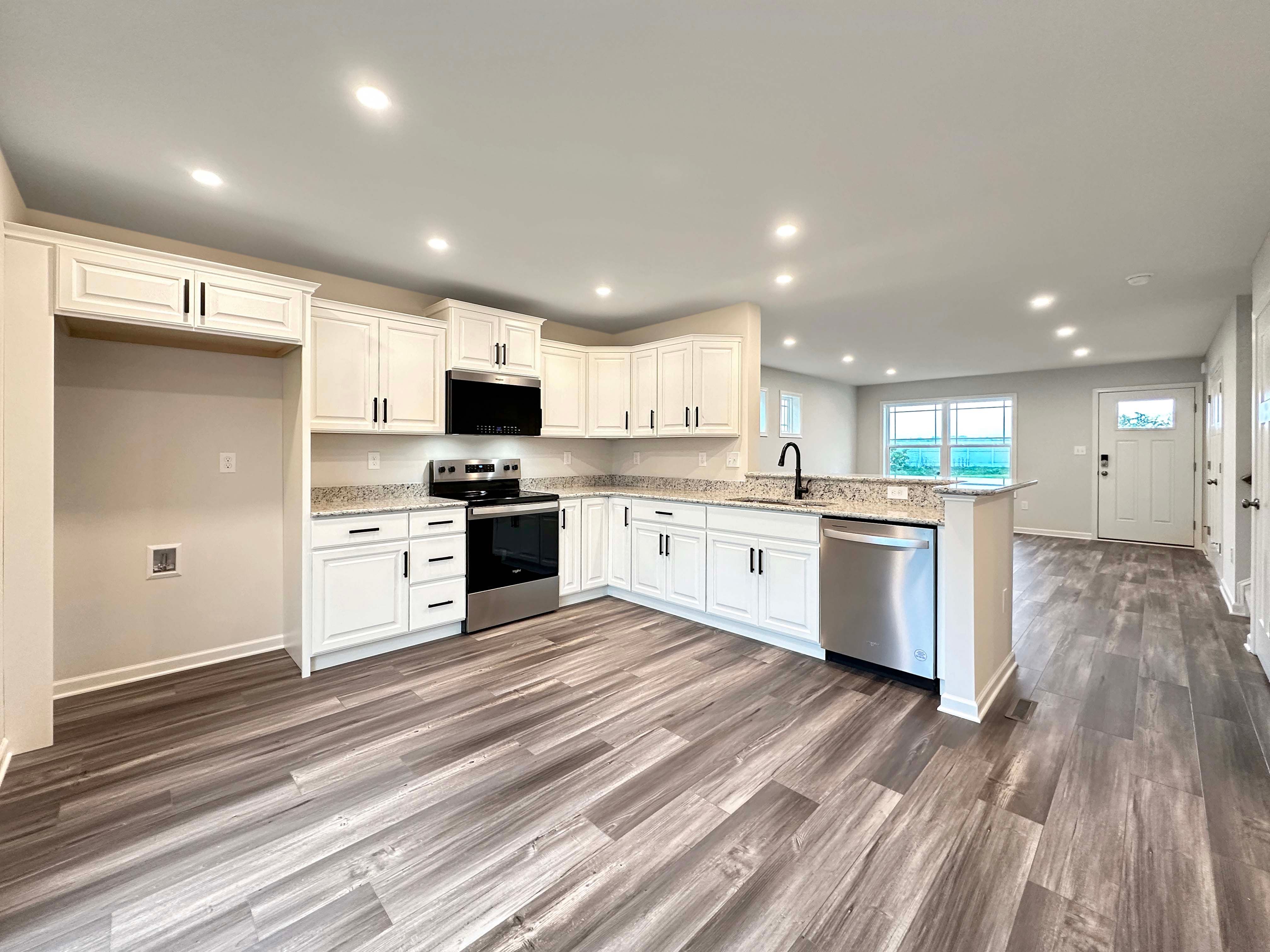 Bright kitchen with recessed lighting and white cabinets, stainless appliances, black hardware, and breakfast bar with overhang.