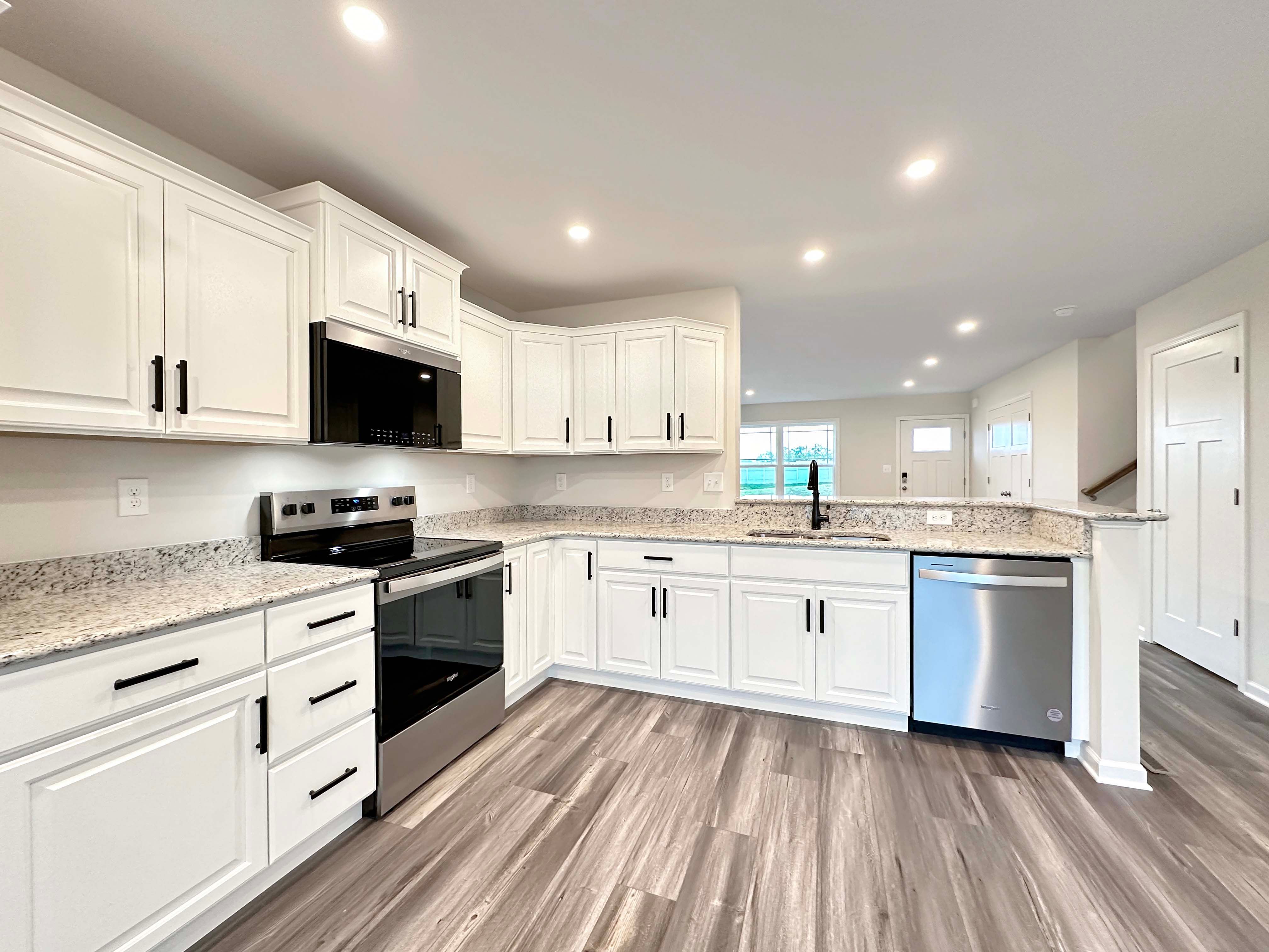Bright kitchen with wood-like flooring, white cabinets, stainless appliances, and black finishes.