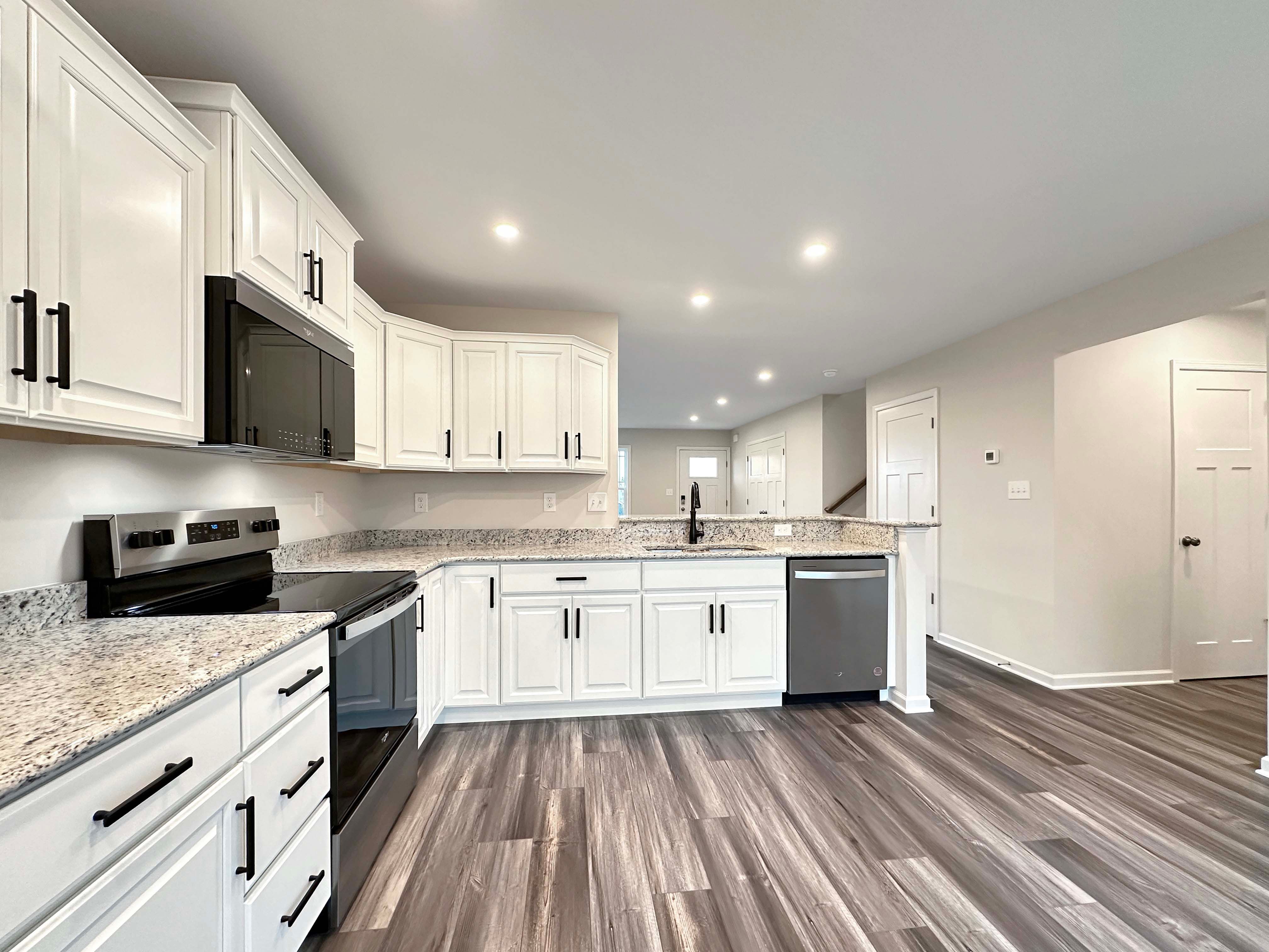 View from the corner of the kitchen including white cabinetry, black hardware, stainless appliances, and recessed lighting