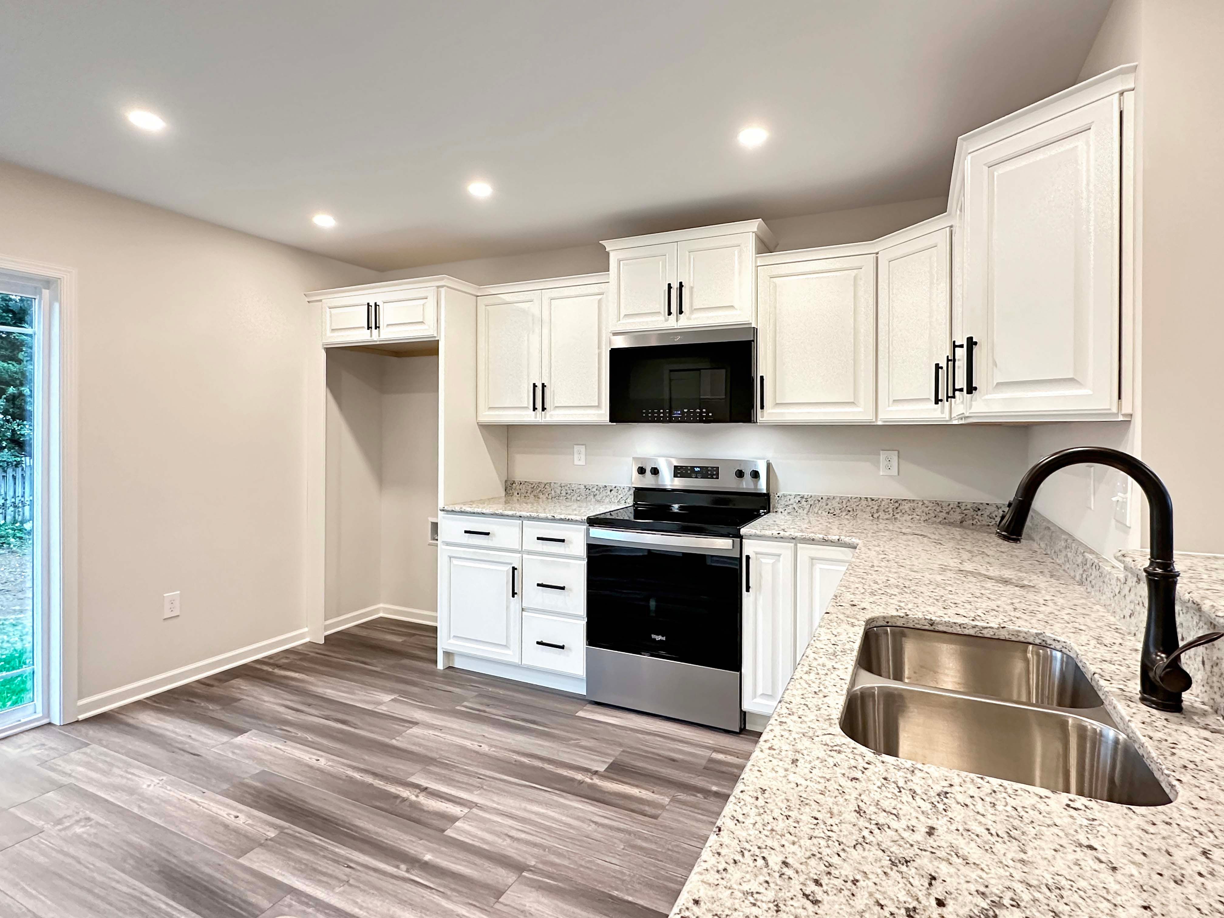 Modern kitchen with a large granite bar, white cabinetry, and a black faucet, overlooking a bright dining area with sliding doors