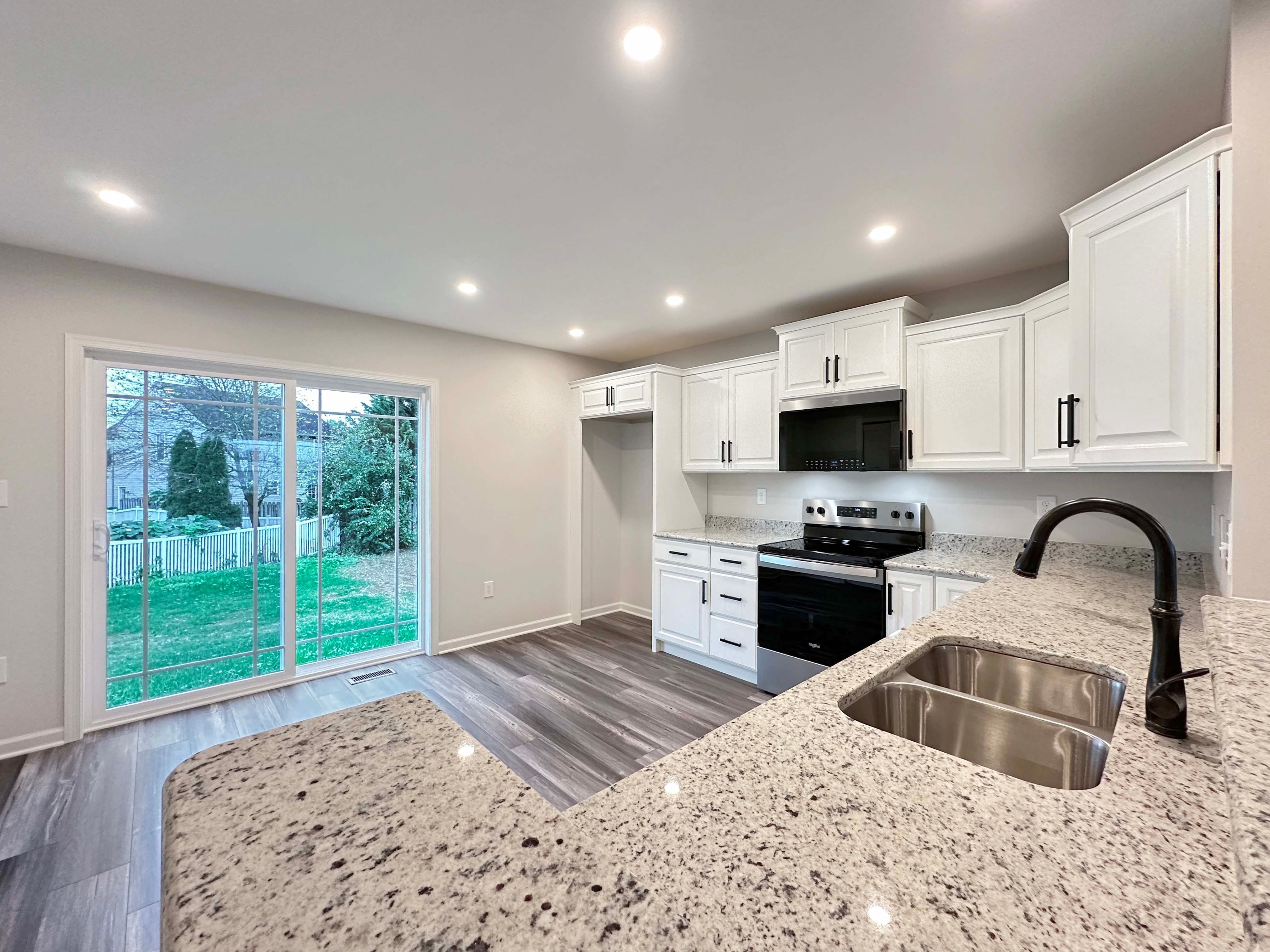 Bright kitchen with white cabinetry, granite countertops, and stainless-steel sink. View of backyard through sliding glass doors