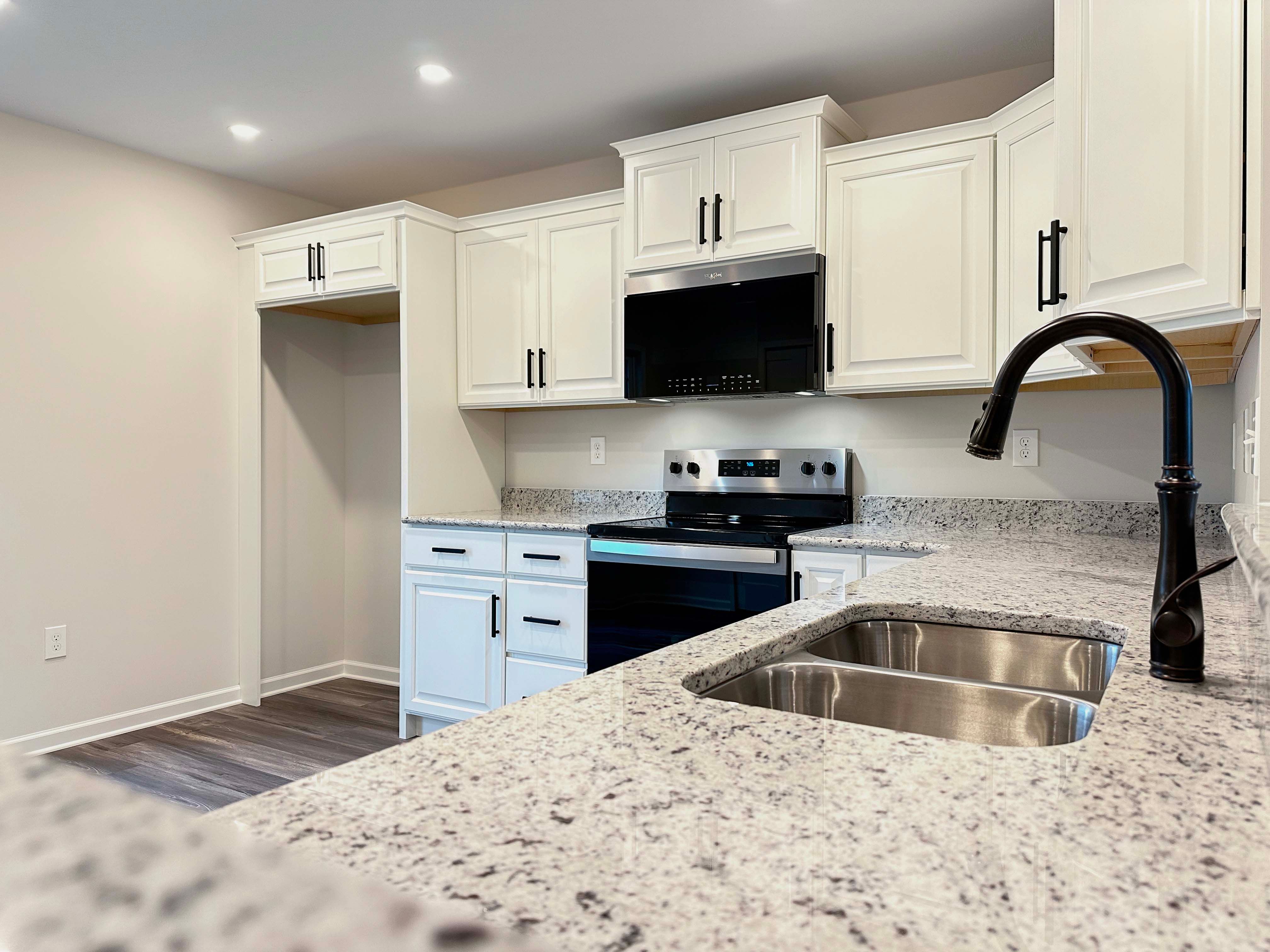 Detailed kitchen shot showcasing the granite countertops, black stainless-steel sink faucet, and modern black appliances.