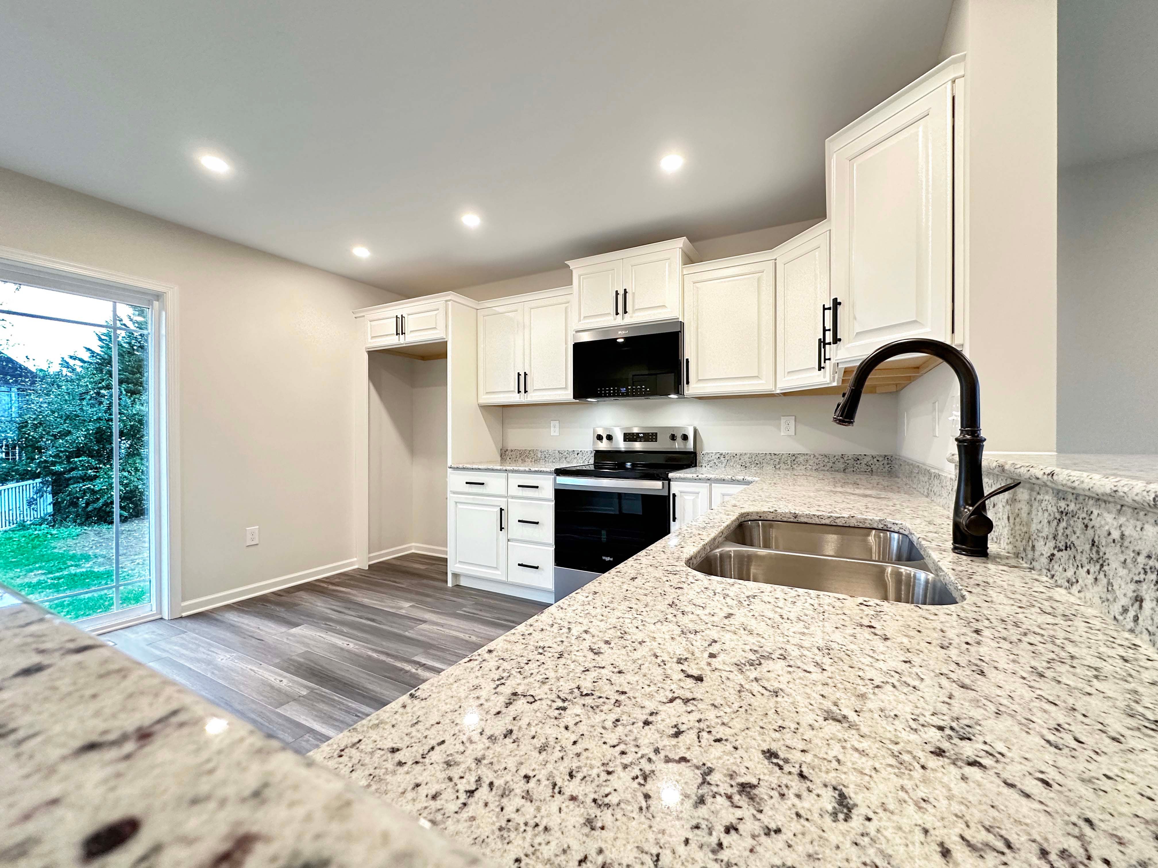Bright kitchen with white cabinetry, granite countertops, and stainless-steel sink. View of backyard through sliding glass doors
