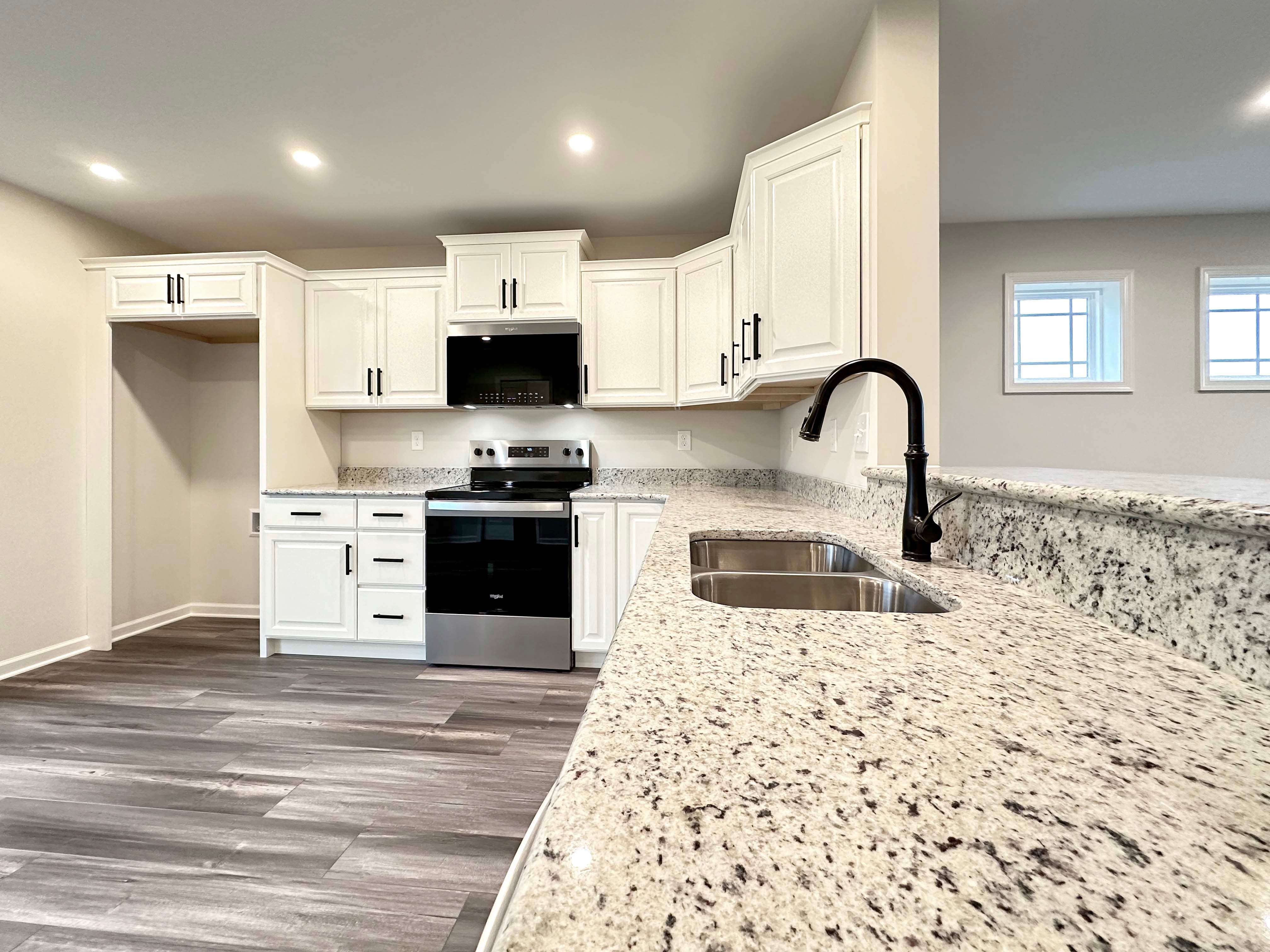 Open kitchen with bright lighting, large granite counters, and a modern black sink faucet, highlighting the cooking area.