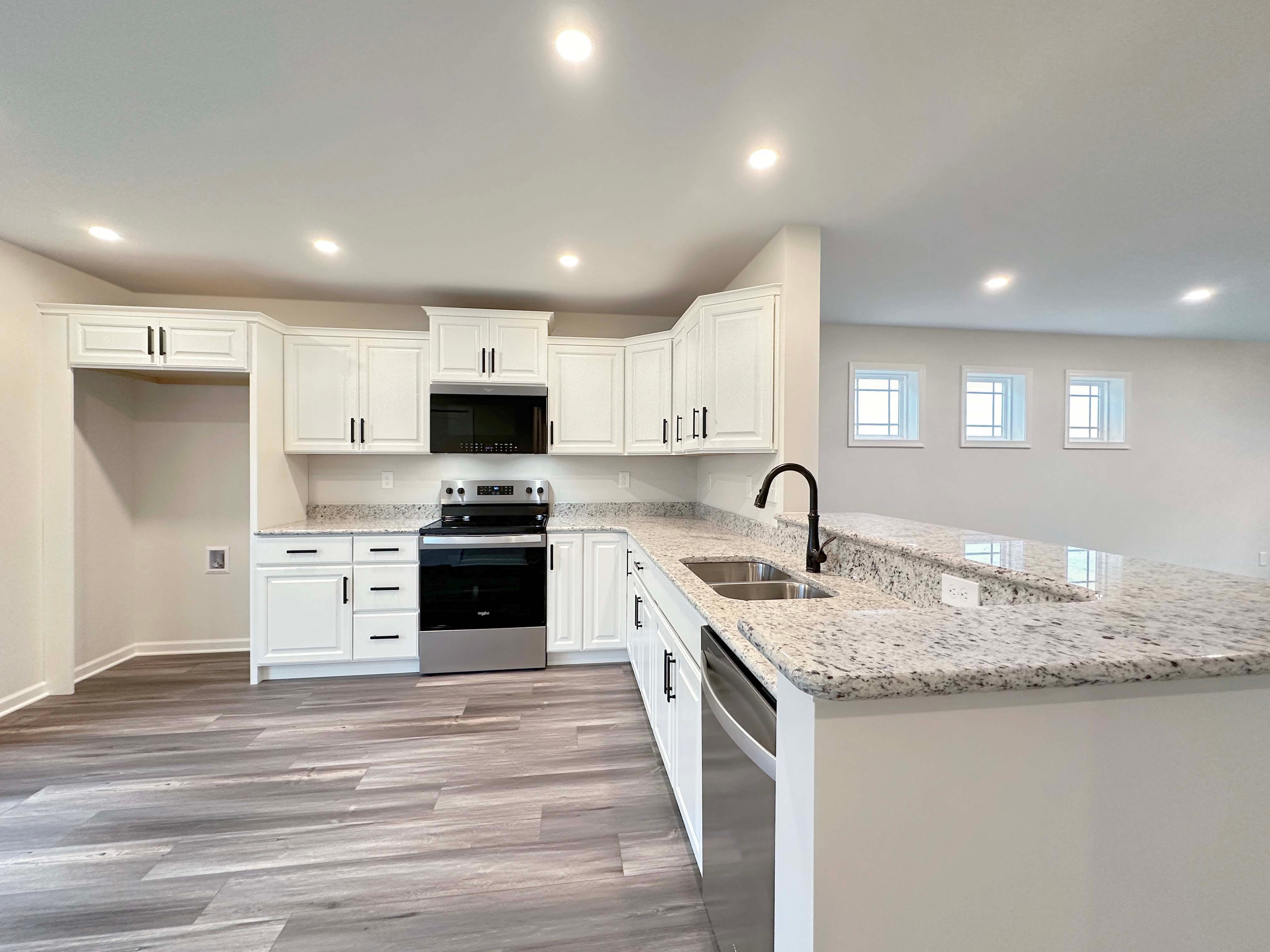 Wide-angle kitchen view with white cabinetry, stainless steel appliances, and large granite countertop with breakfast bar.