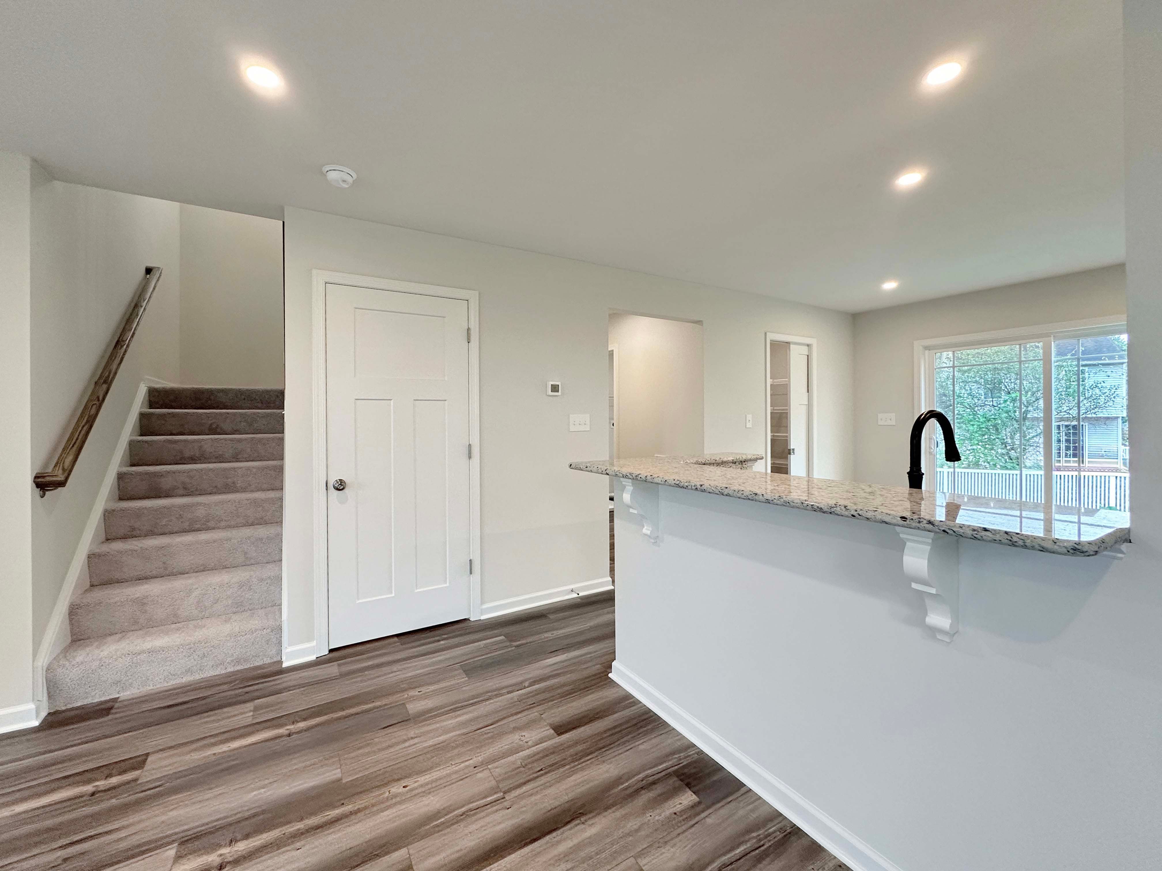 Open living space with large windows, natural light, and gray-toned wood-look flooring, view toward kitchen.