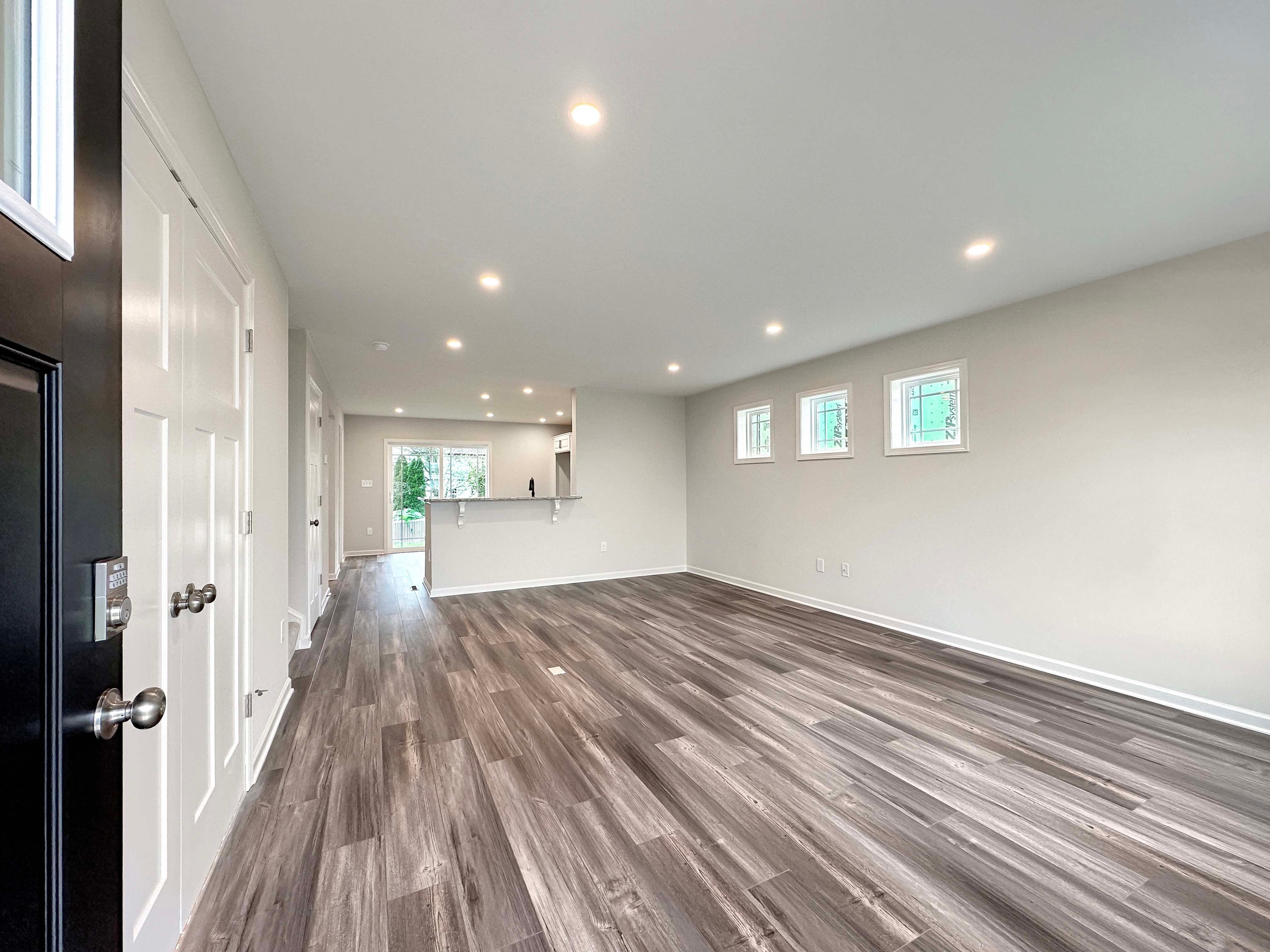 Wide view of open-concept living room and kitchen with light wood-look flooring and recessed lighting.