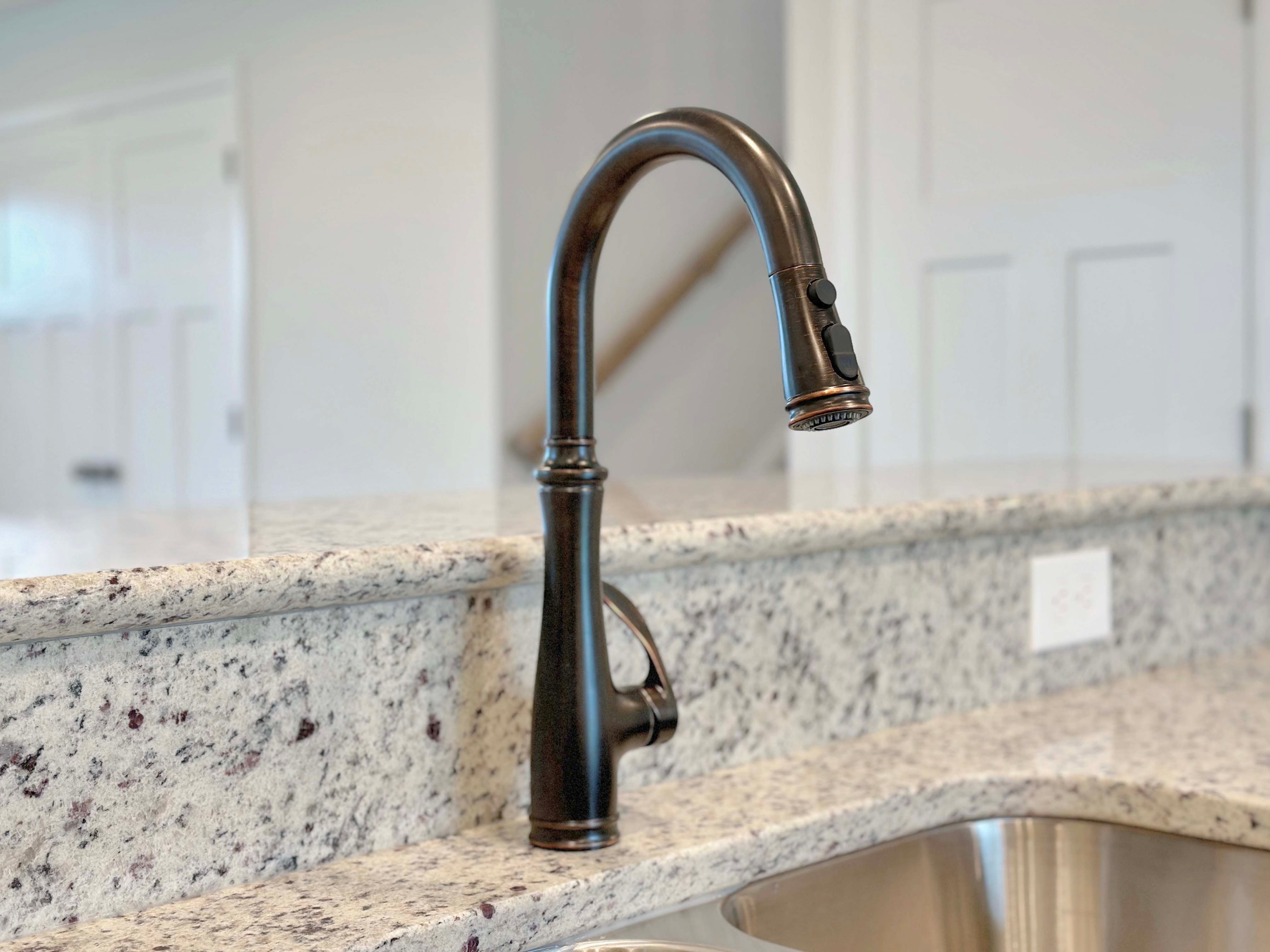 Detailed shot of the oil-rubbed bronze kitchen faucet and undermount sink with gleaming granite countertops.
