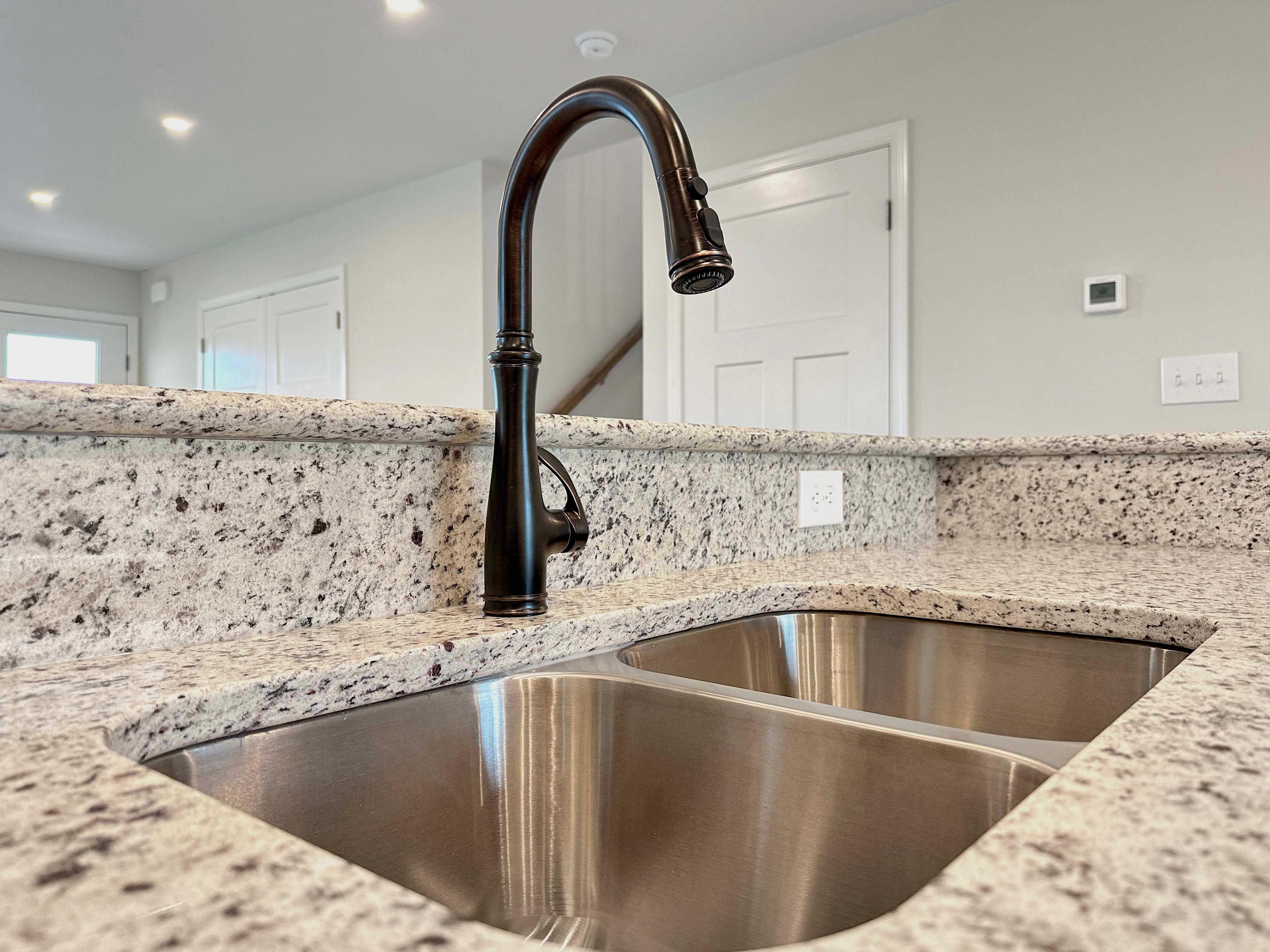 Close-up view of the oil-rubbed bronze kitchen faucet over a double-basin sink set into granite countertops.