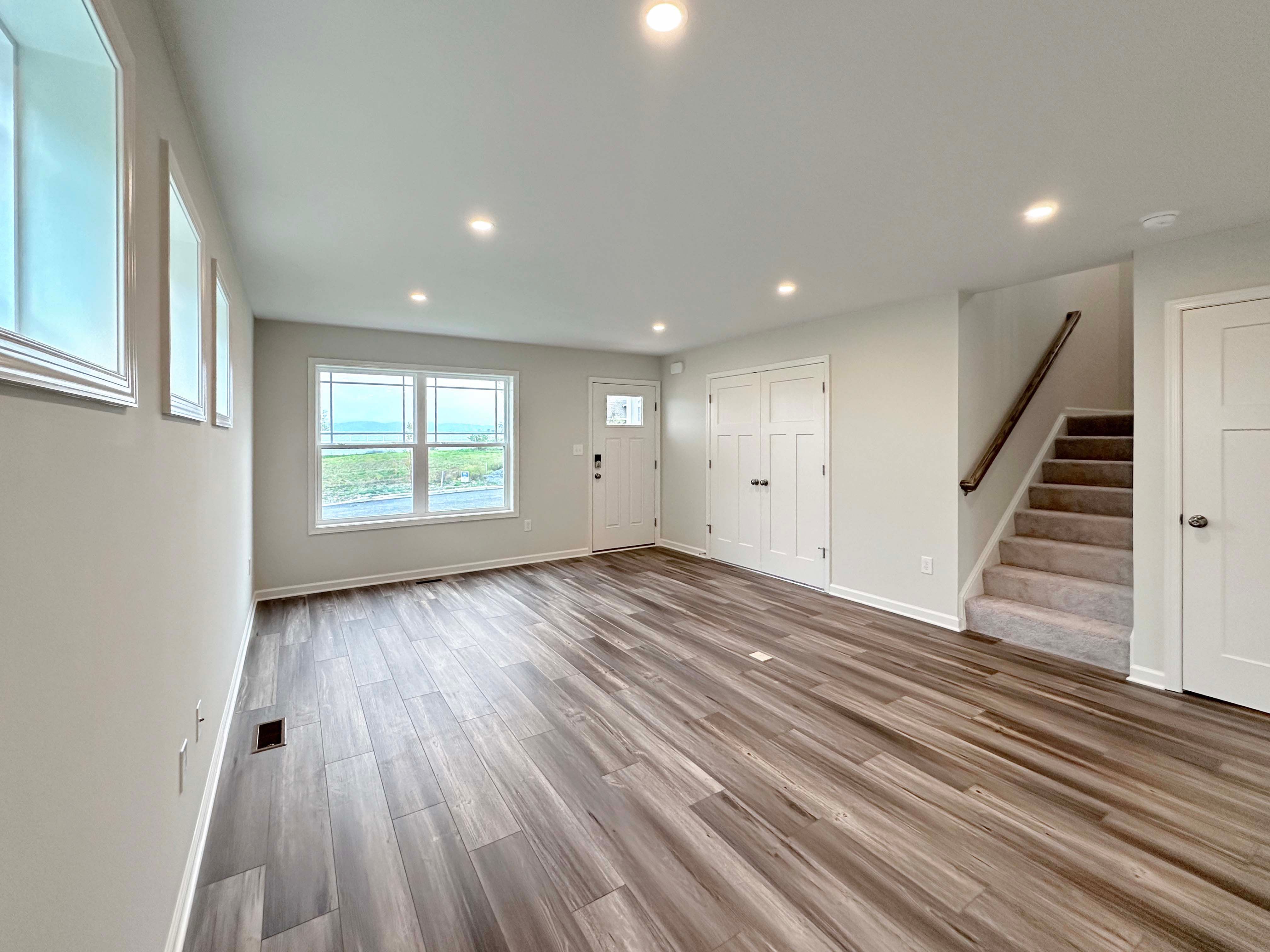 Open-concept living room with large windows and wood-look flooring, view of unfurnished space and stairs.