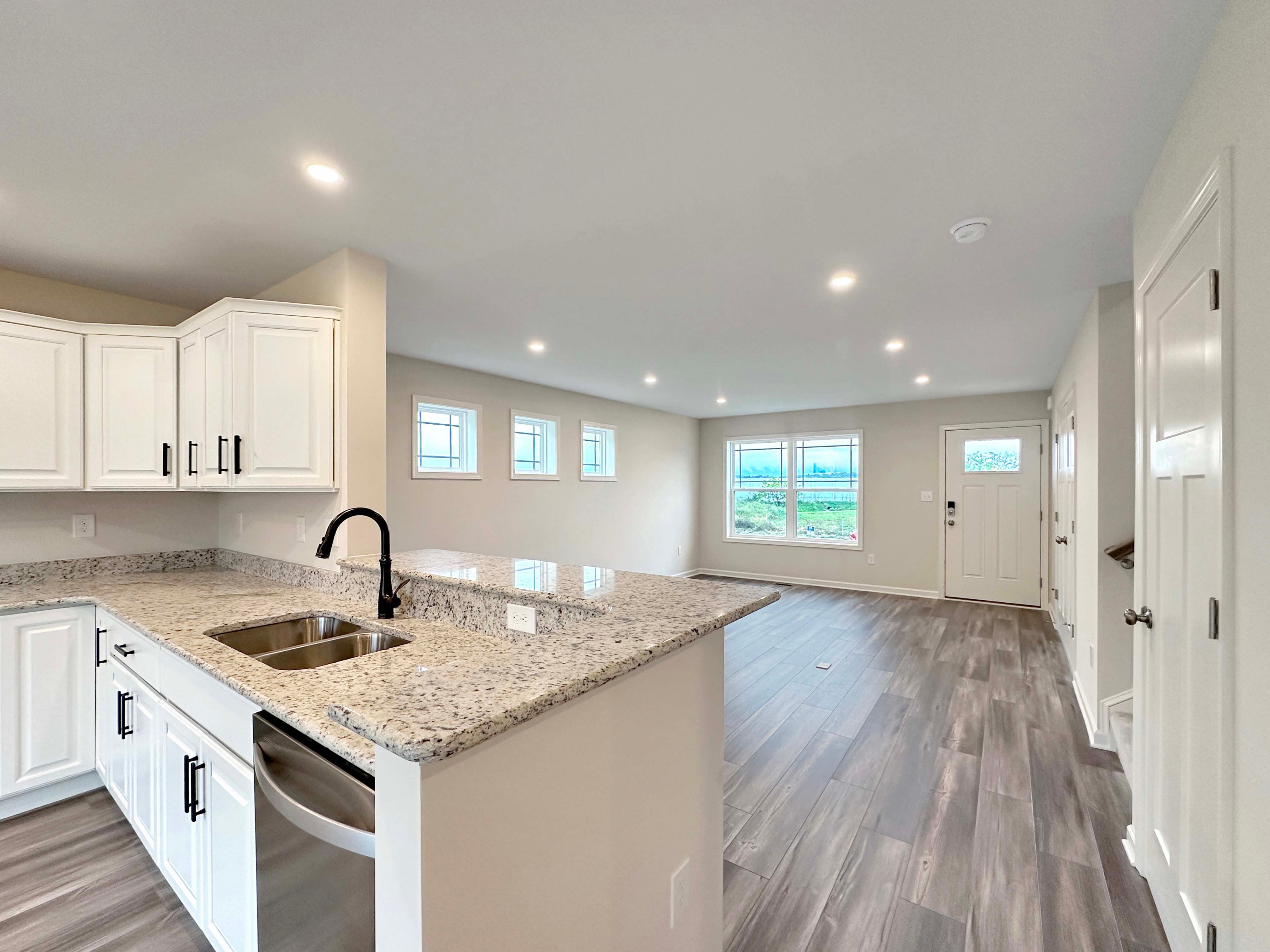 Modern open kitchen and living room with light gray wood-look floors, white cabinets, and granite countertops
