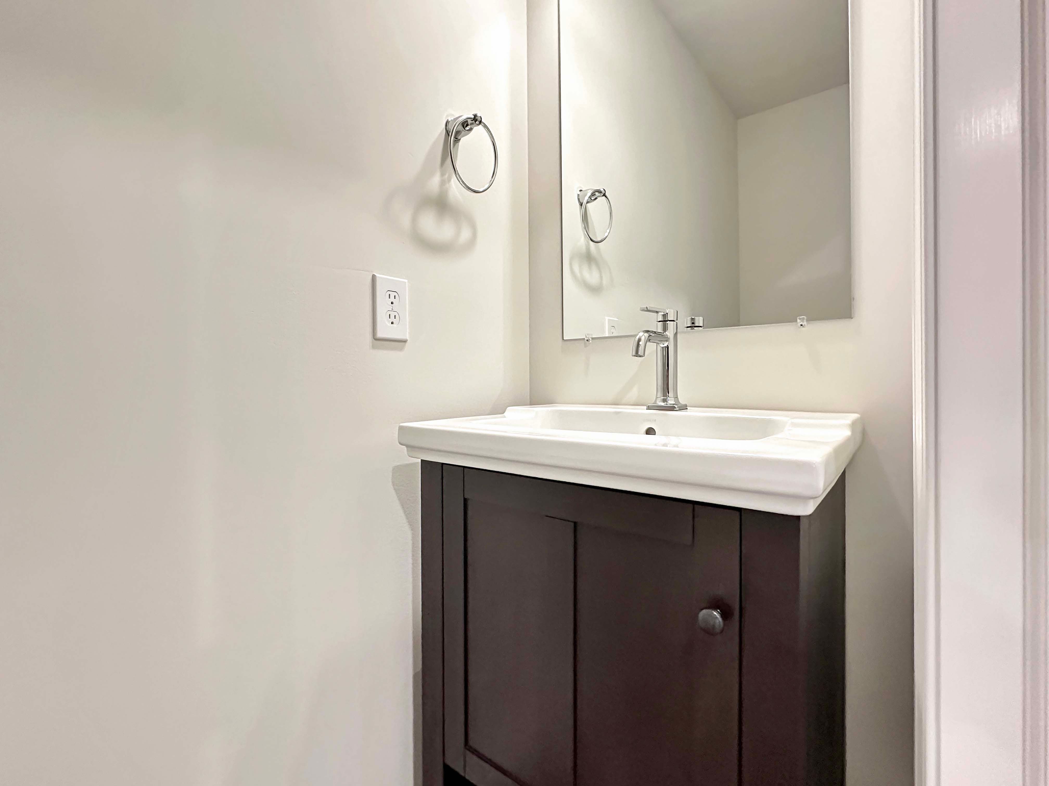 Powder room with dark wood vanity, white countertop, and a rectangular mirror above the sink.