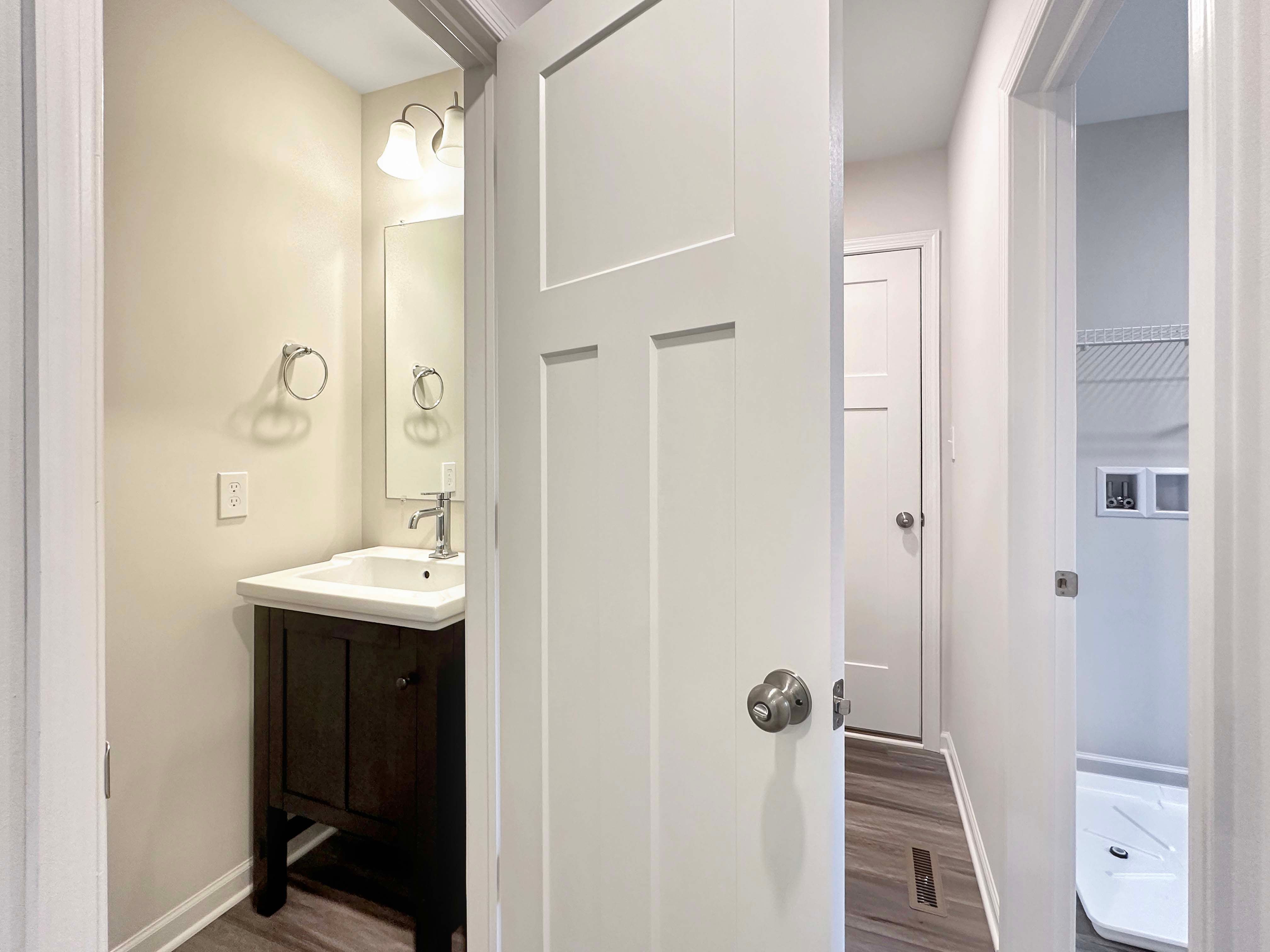 Hallway view of a powder room with white vanity and adjacent laundry room featuring hookups for washer and dryer.