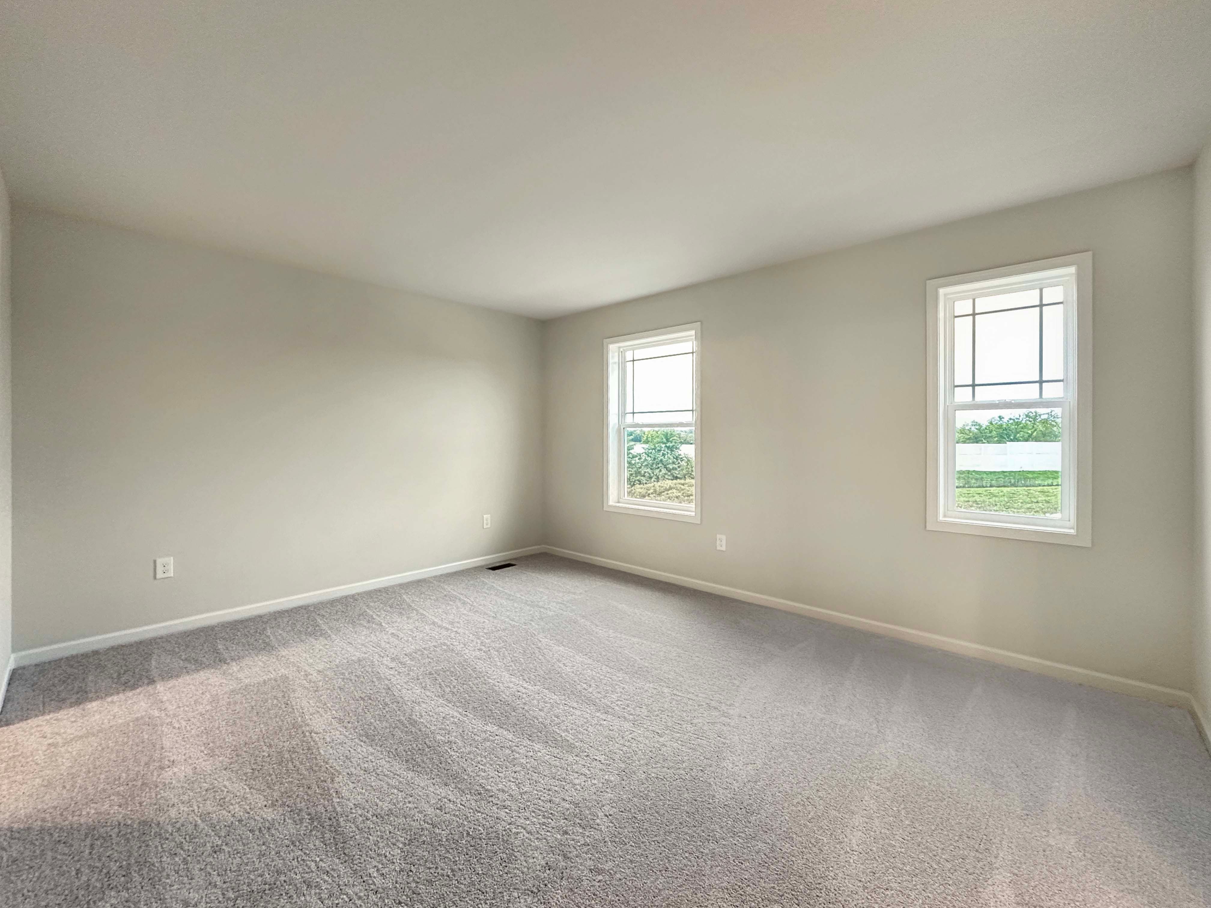 Spacious owner's bedroom with two windows and plush carpet flooring
