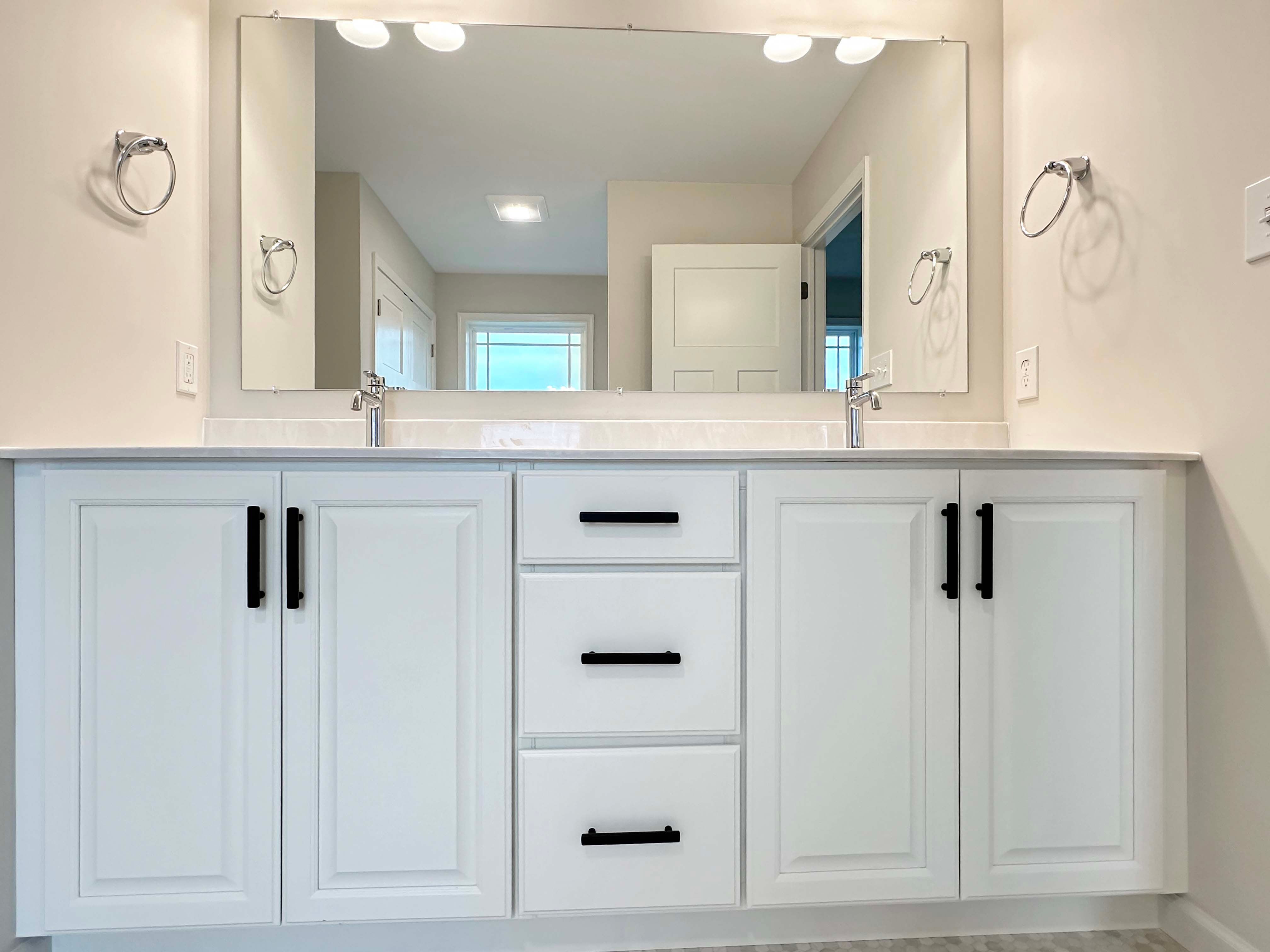 Close-up of the owner's bath vanity with dual sinks, white cabinets, and modern black hardware.