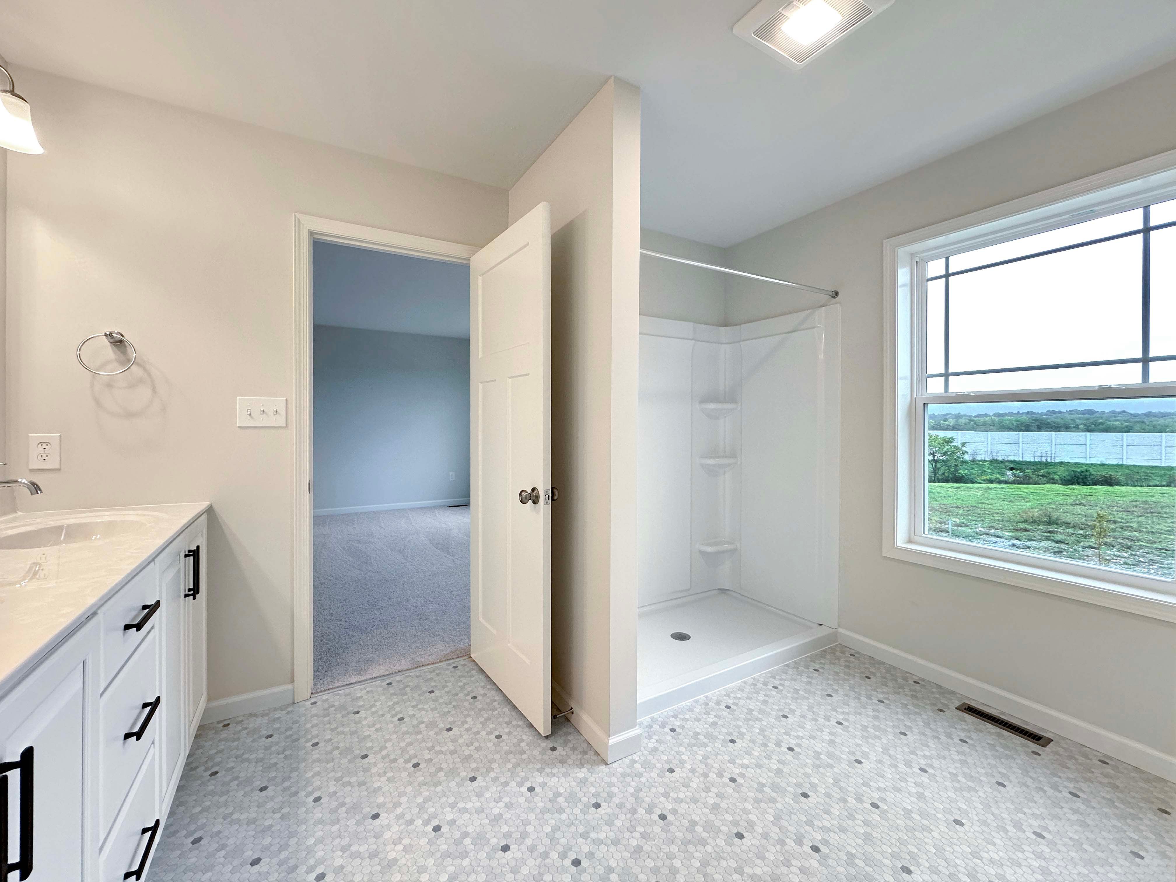 Owner's bathroom with a walk-in shower, large window, and sleek vanity, providing a bright, open feel.