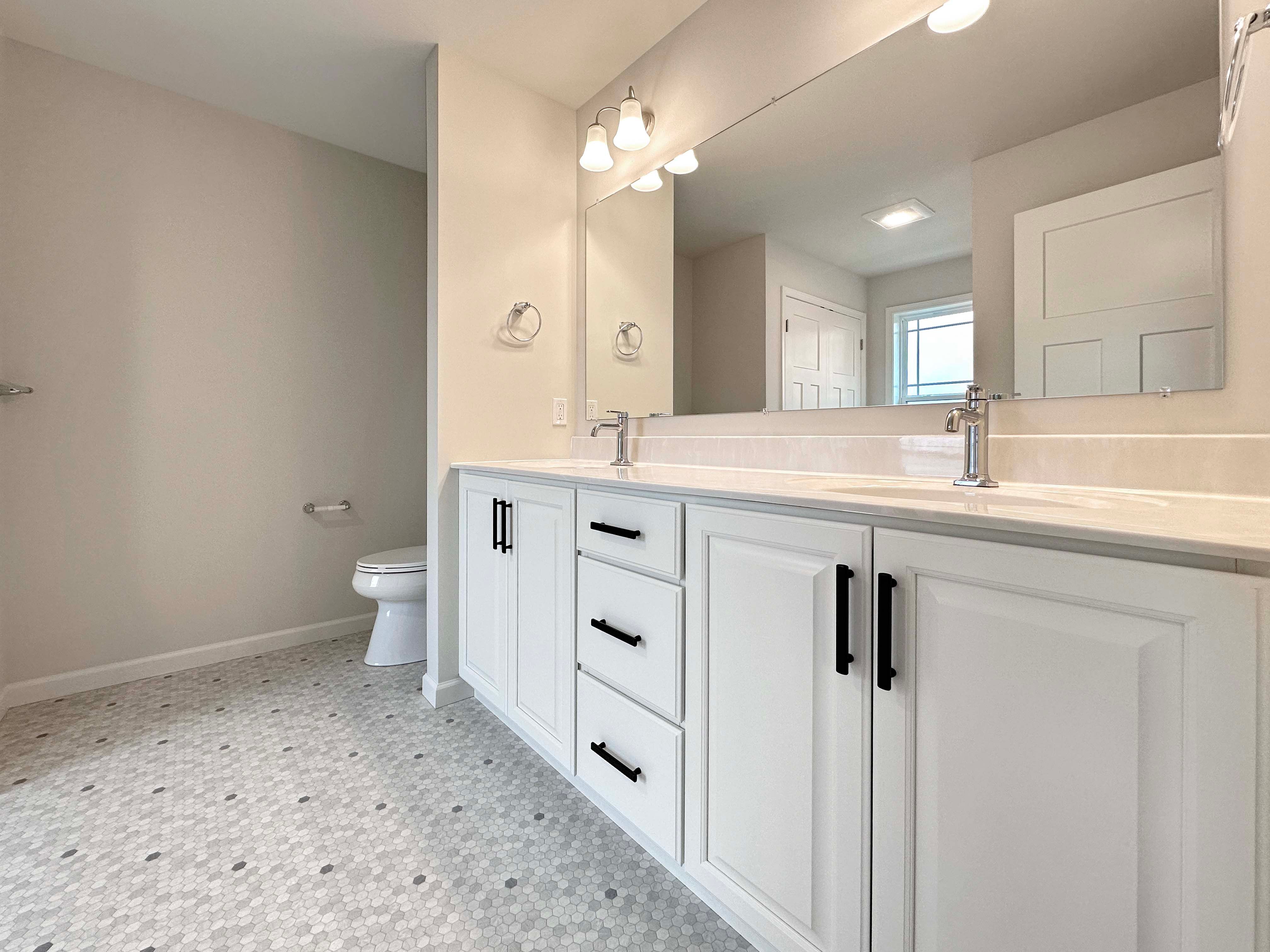 Spacious owner's bath with a large double vanity, white cabinets, and a modern hexagon tile floor.