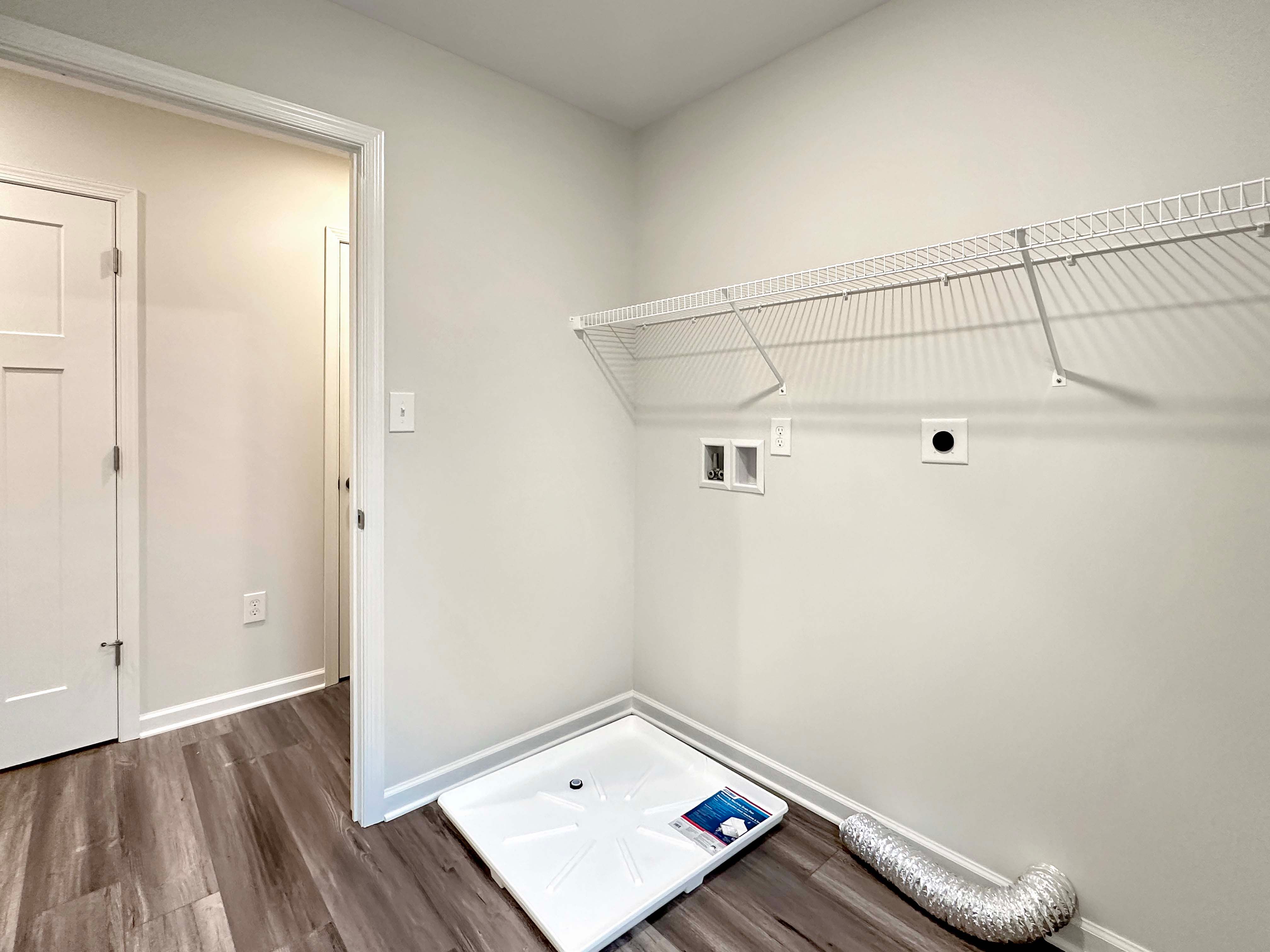 Spacious laundry room with hardwood floors, washer and dryer hookups, and shelving for added storage.